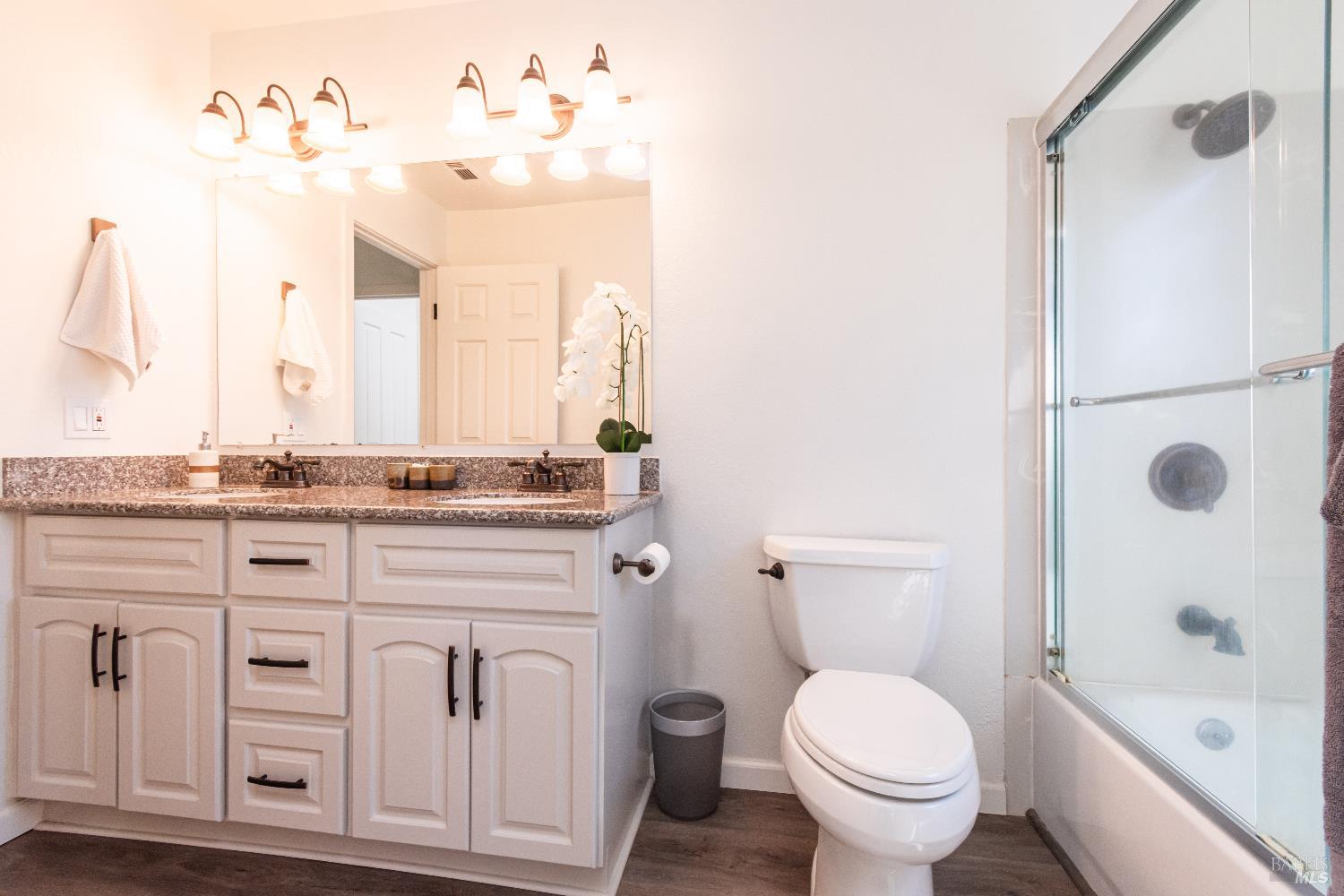 Bathroom with a double-sink vanity and glass-enclosed tub and shower.