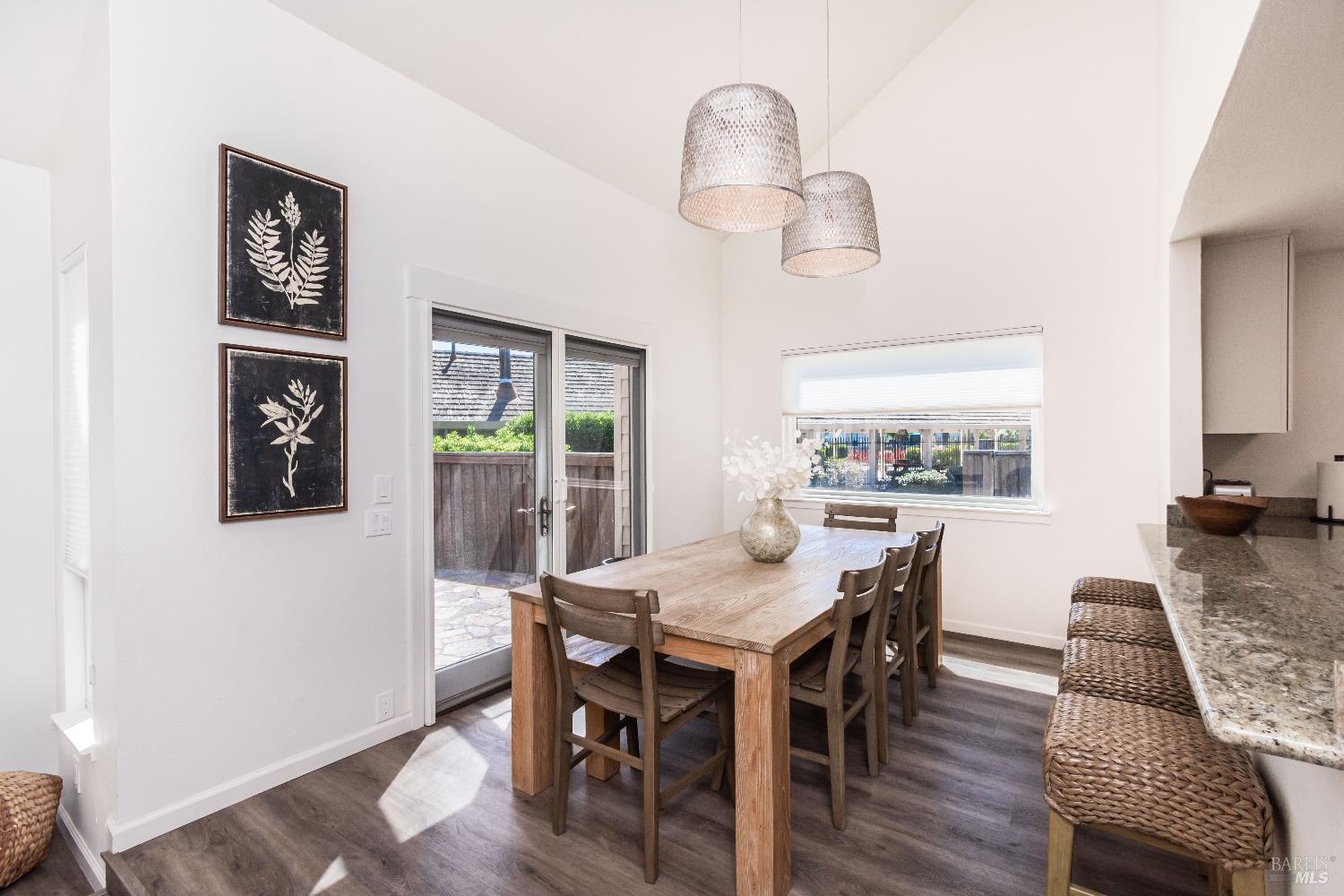 Dining area with a long wooden table, woven pendant lights, and sliding glass doors to a patio.