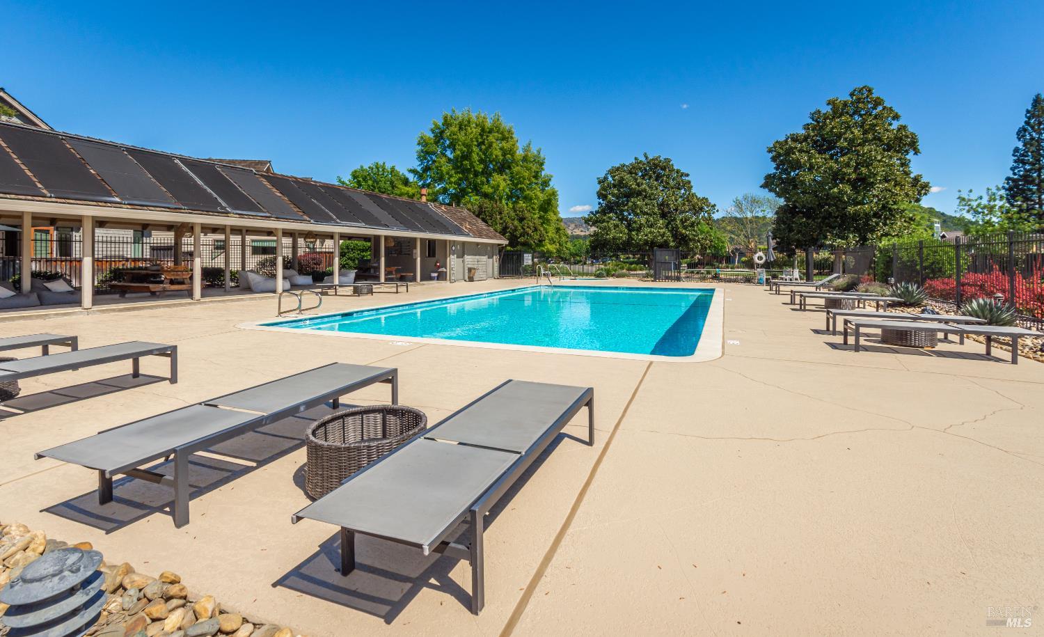 Outdoor pool with lounge chairs beside a covered patio topped with solar panels.
