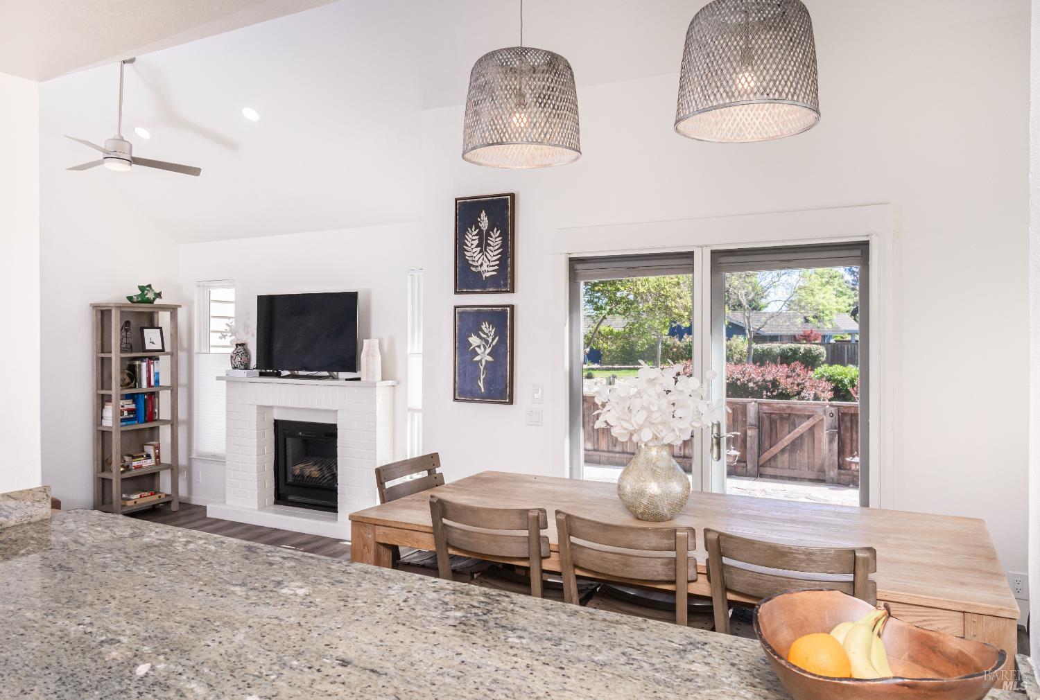 Dining area with a long wooden table, woven pendants, fireplace, and glass doors to a garden.