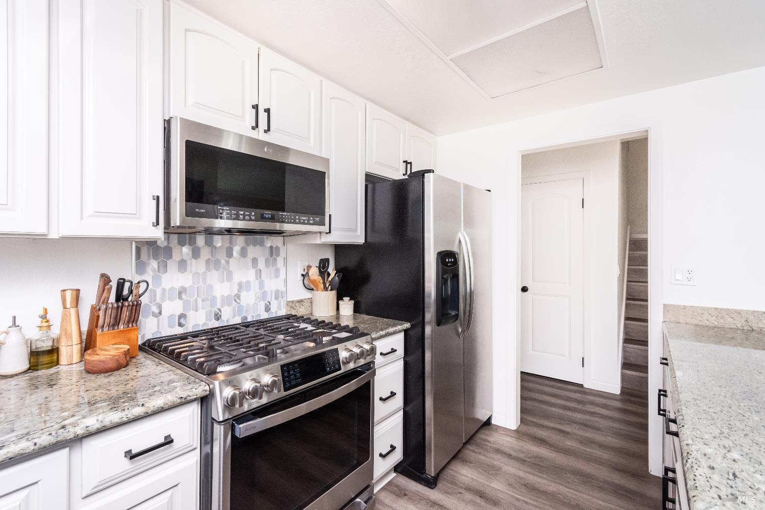 Kitchen with white cabinets, granite counters, hexagonal tile backsplash, and stainless steel appliances.