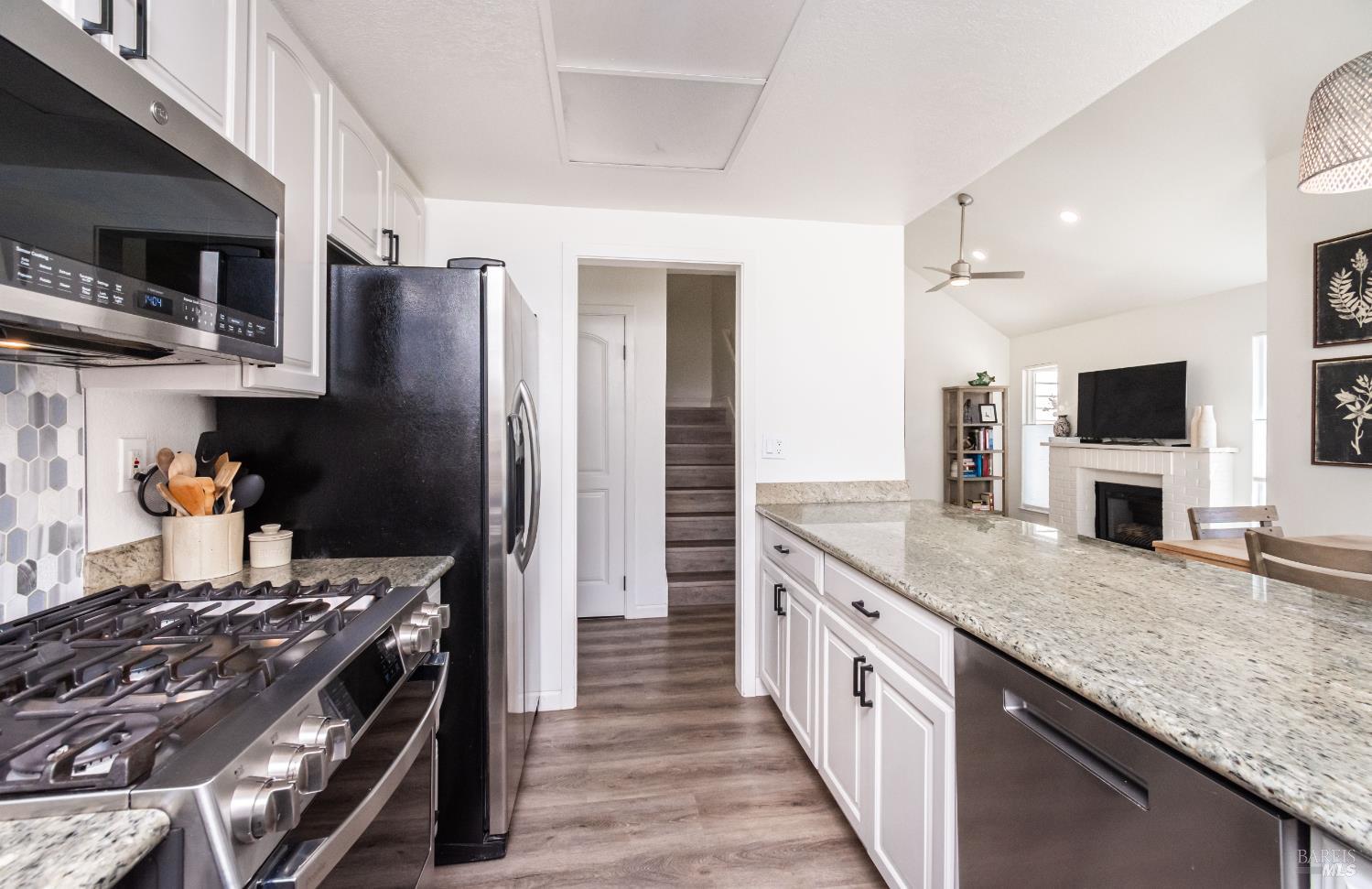 Kitchen with a granite island, stainless steel appliances, and an adjoining living room with a fireplace.