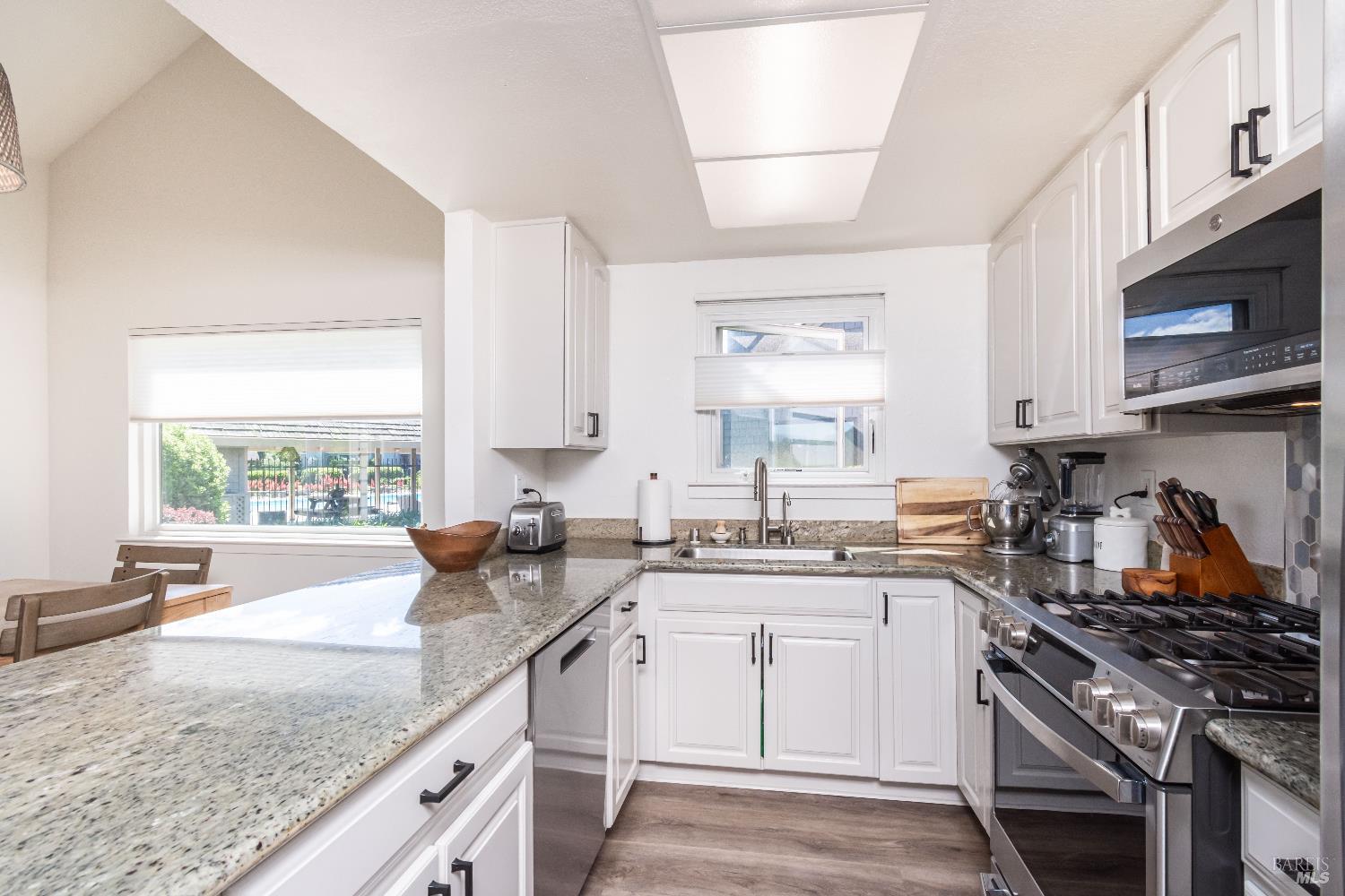 Kitchen with white cabinetry, granite counters, and stainless steel appliances beside a window.