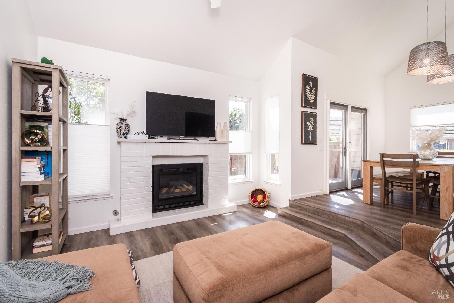 Living room with a white brick fireplace, vaulted ceiling, and adjoining dining area.