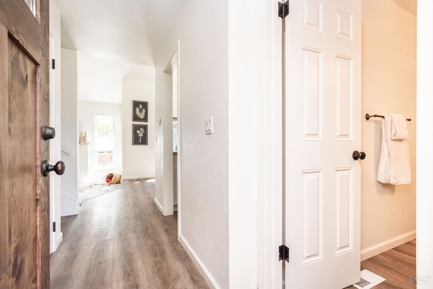 Bright hallway with wide-plank floors, a dark wood entry door, and an open white paneled door.