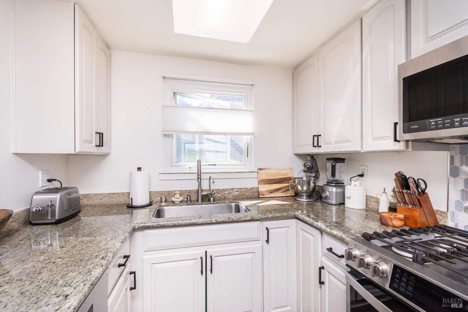 Bright kitchen with white cabinets, speckled stone counters, a window over the sink, and a stainless gas range.