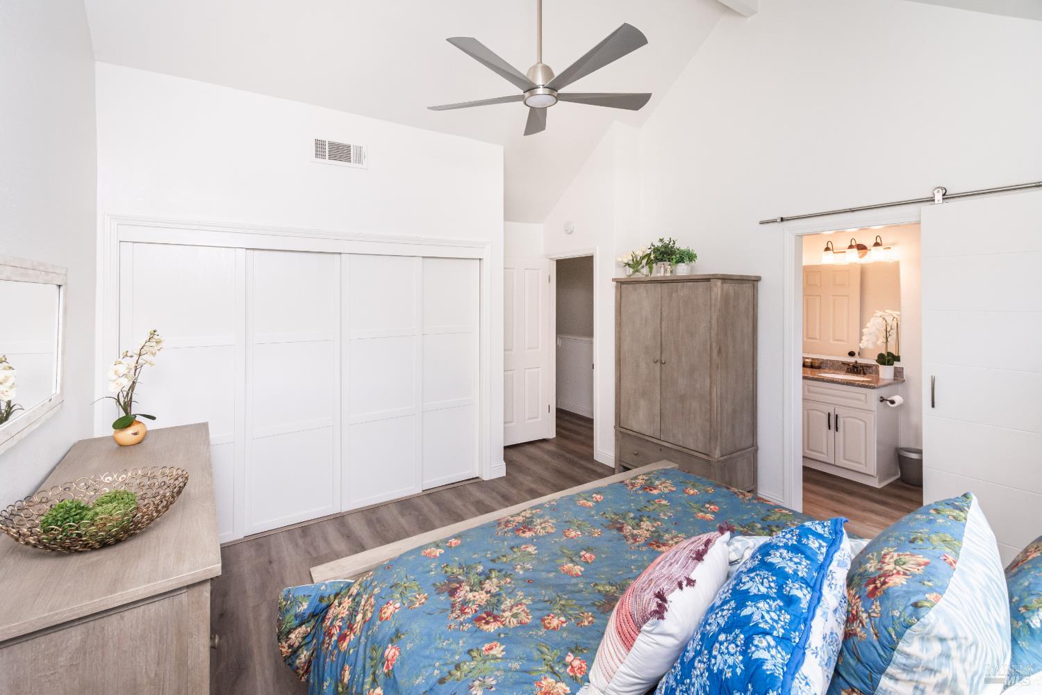 Bedroom with a blue floral bedspread, white sliding closet doors, and a wood-finish armoire.