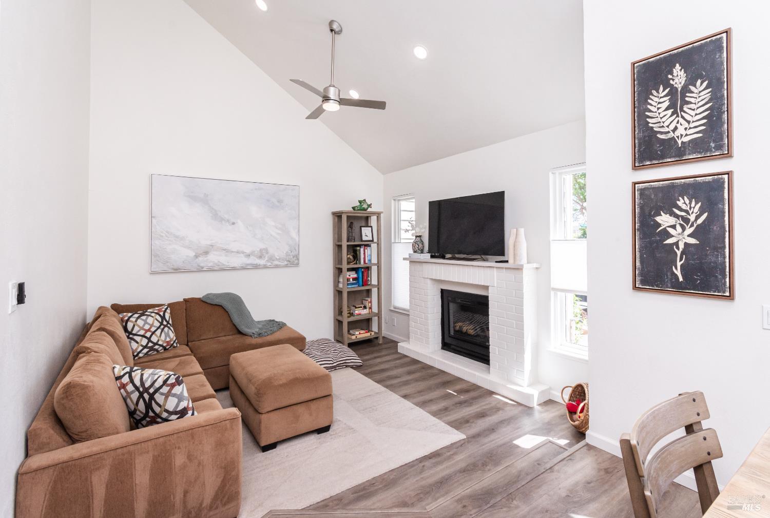 Living room with a vaulted ceiling, brown sectional sofa, and white brick fireplace.