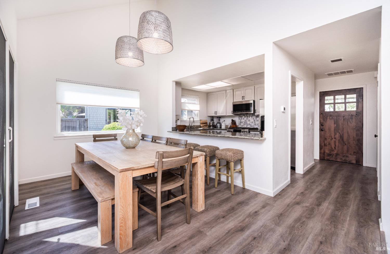 Dining area with a wooden table and bench beside an open kitchen and breakfast bar.