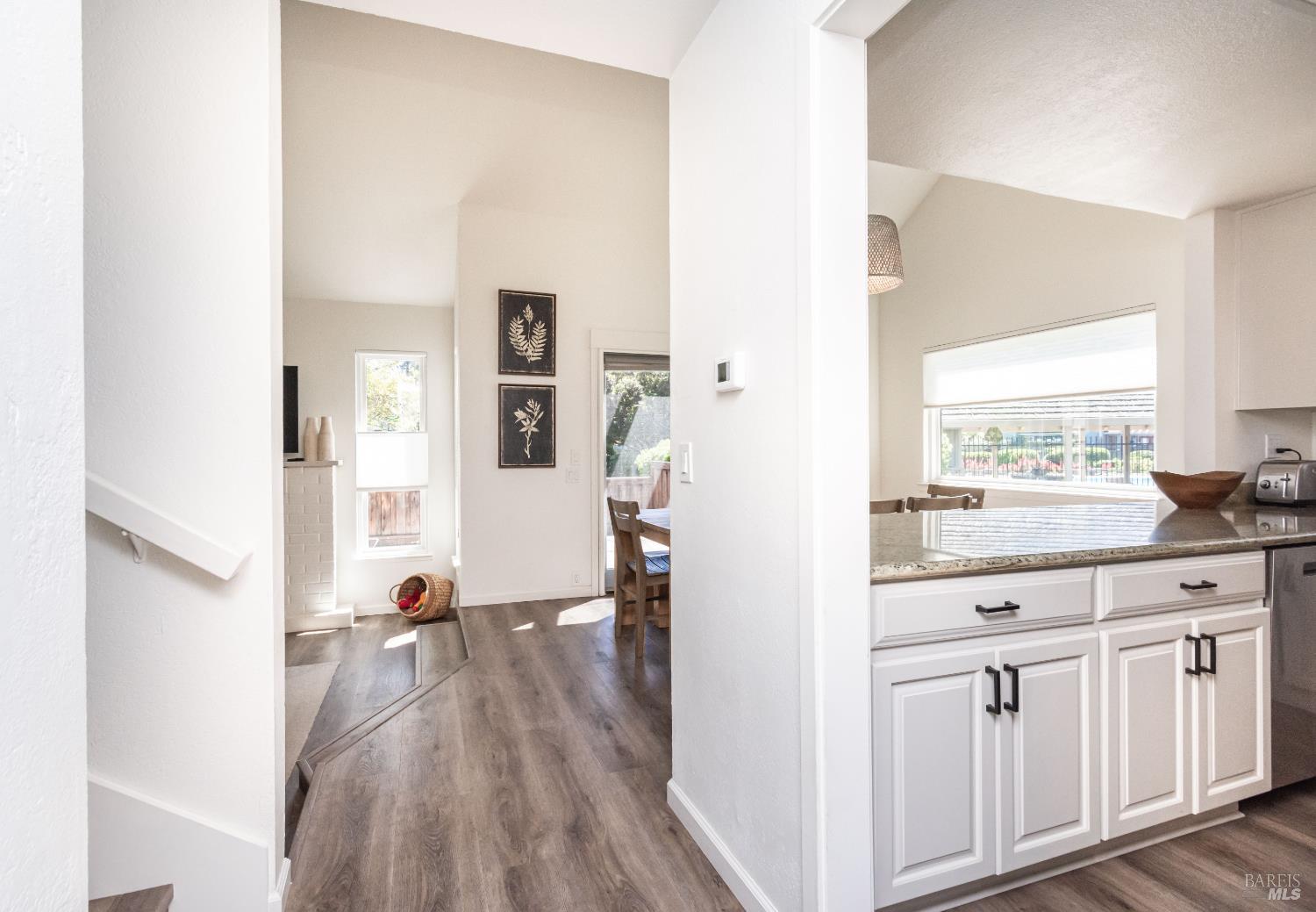 Open-plan kitchen and dining area with white cabinetry, dark floors, and a wide window.