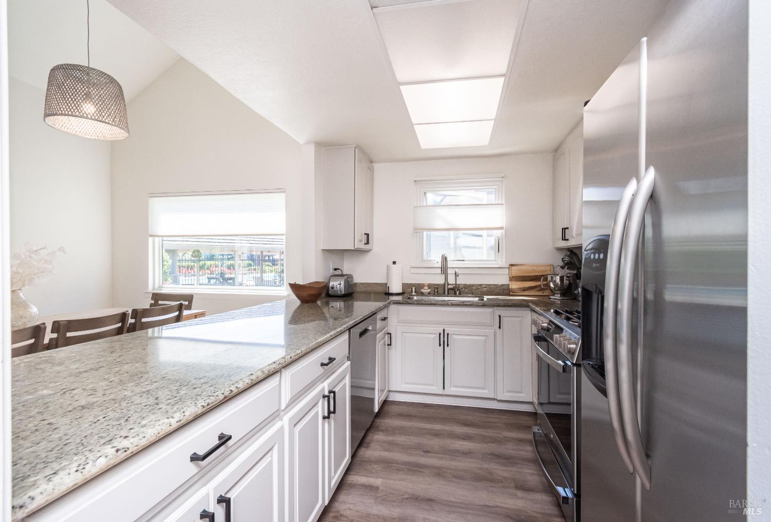 Kitchen with white cabinets, granite counters, stainless steel appliances, and a dining area by the window.
