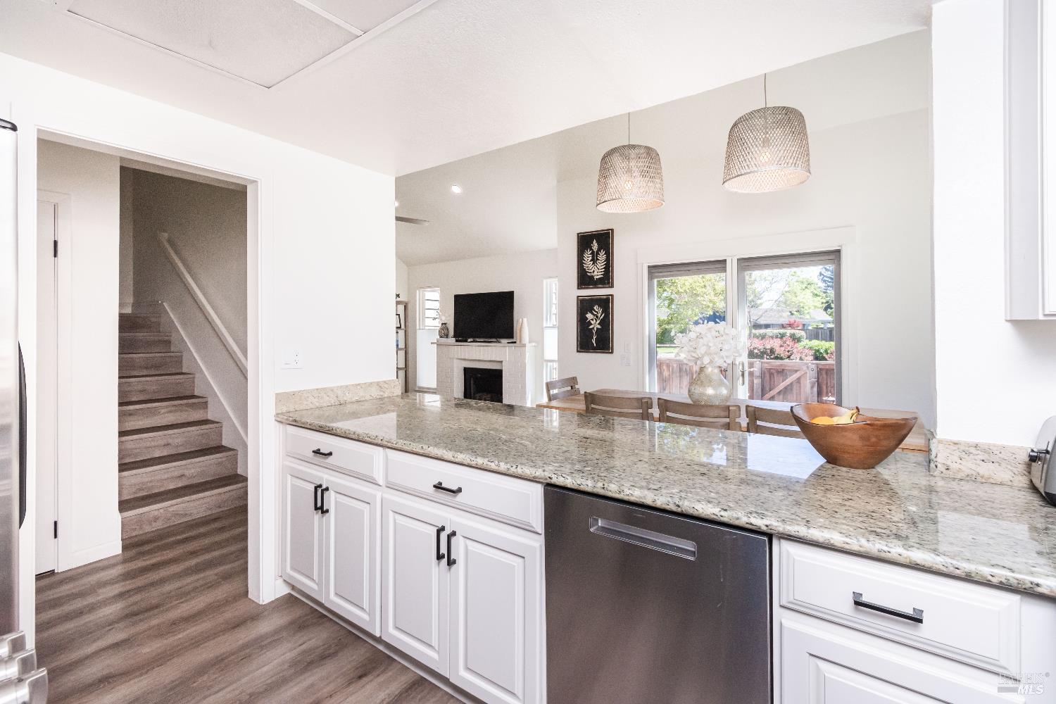 Kitchen with a granite island, pendant lights, and an open view to the living room and fireplace.