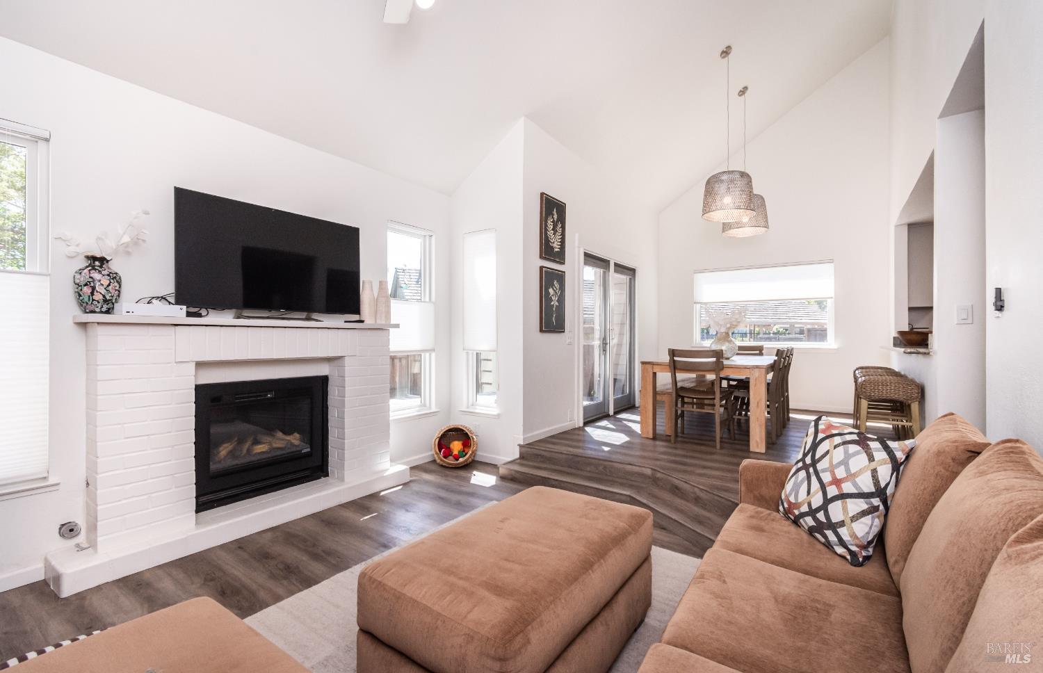 Living room with a white brick fireplace, tan sectional, and dining area beyond.