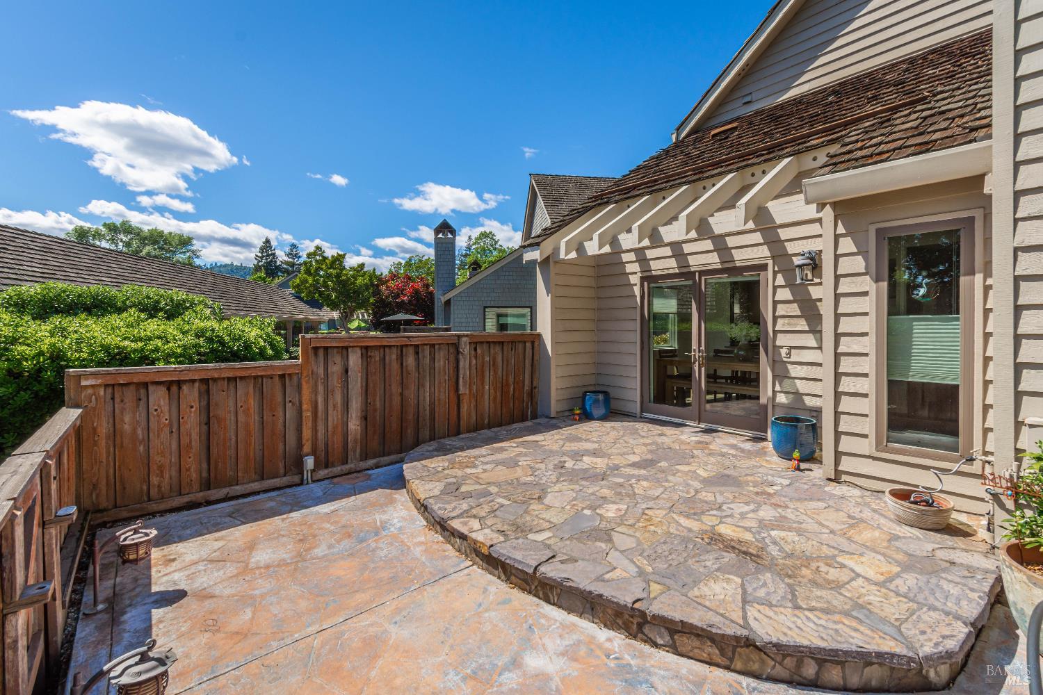 Stone patio beside a tan-sided home, with a wooden fence and glass doors.