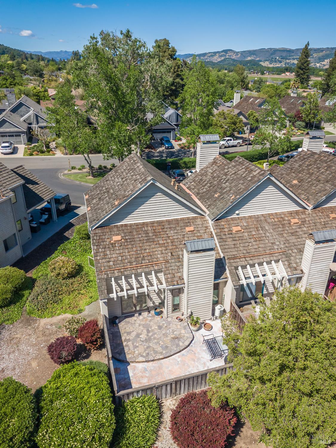 Aerial view of a gray home with a stone patio, landscaped yard, and hills in the distance.