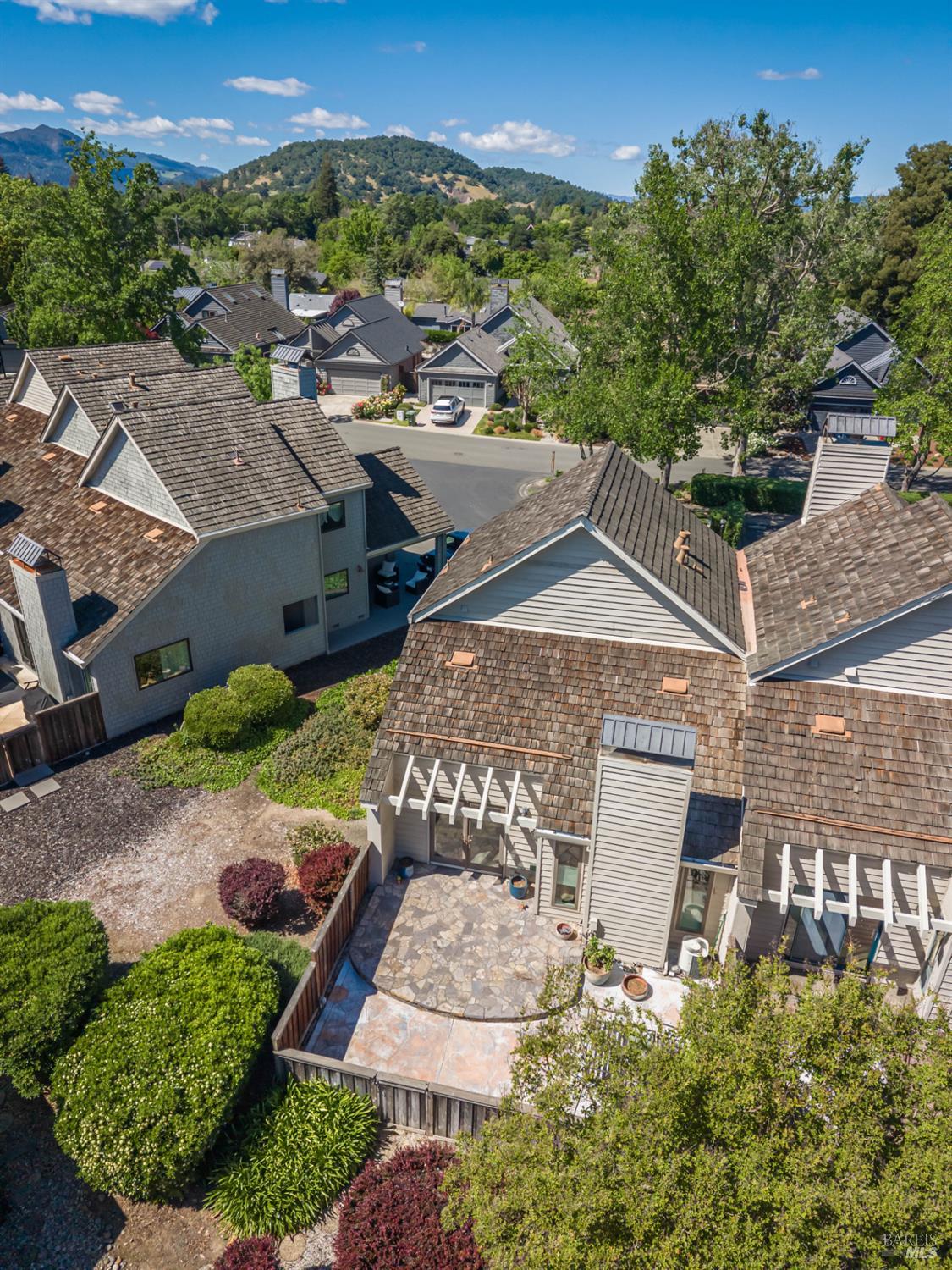Aerial view of a home with a stone patio, landscaped yard, and distant hills.