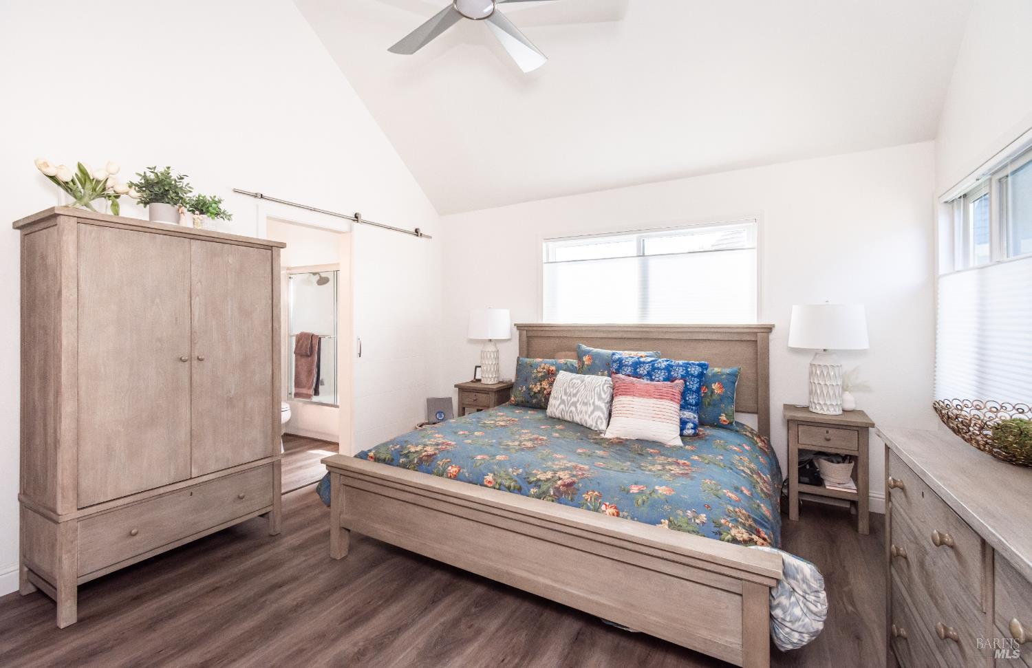 Bedroom with blue floral bedding, matching wood furniture, vaulted ceiling, and bathroom doorway.