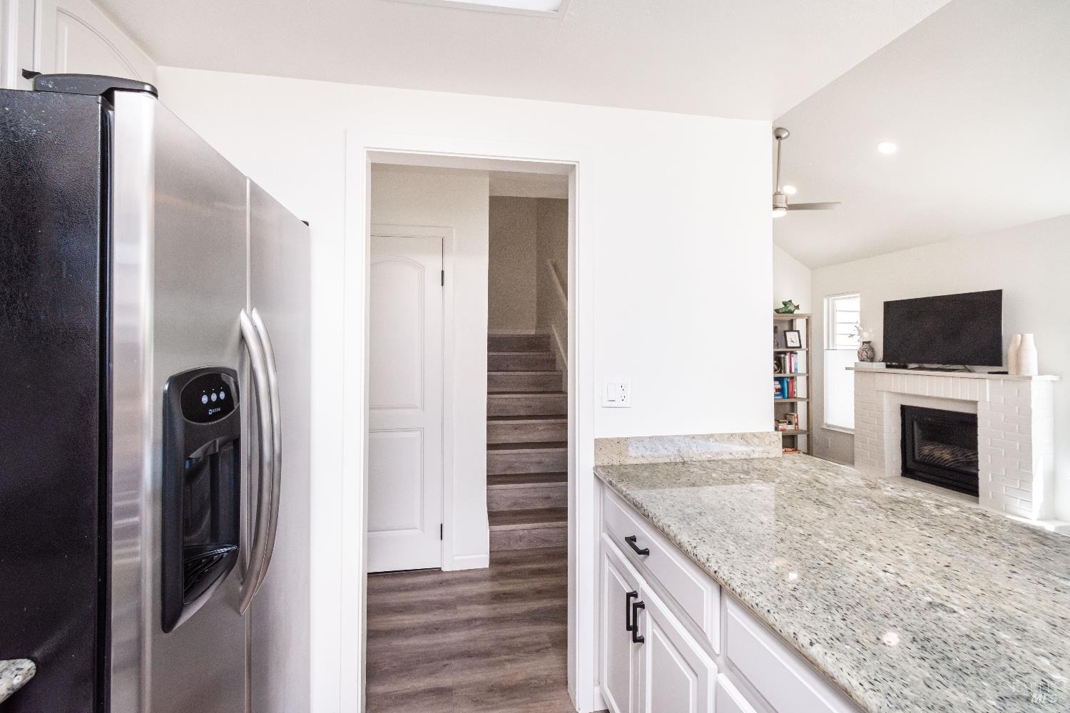 Kitchen with granite island and stainless refrigerator opening onto a living room with fireplace.