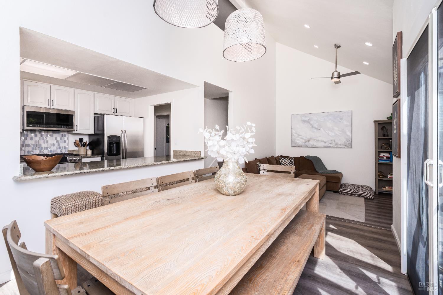 Open-plan dining area and kitchen with a large pale wood table, white cabinetry, and a brown sectional sofa.
