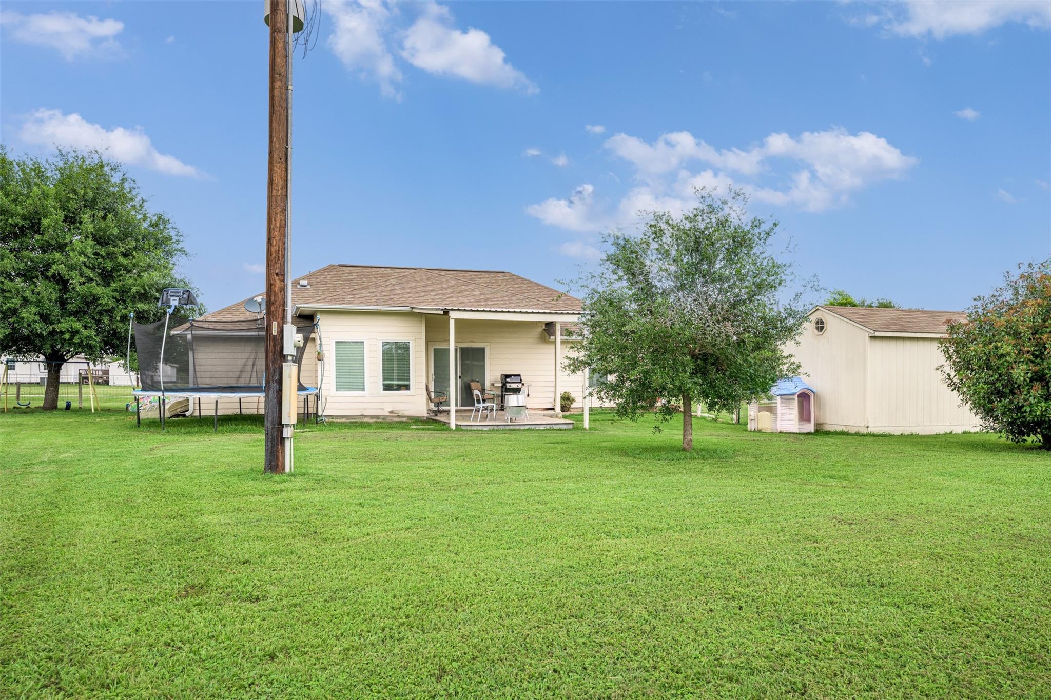 Rear of a single-story home with a covered patio, detached shed, and trampoline across a broad lawn.