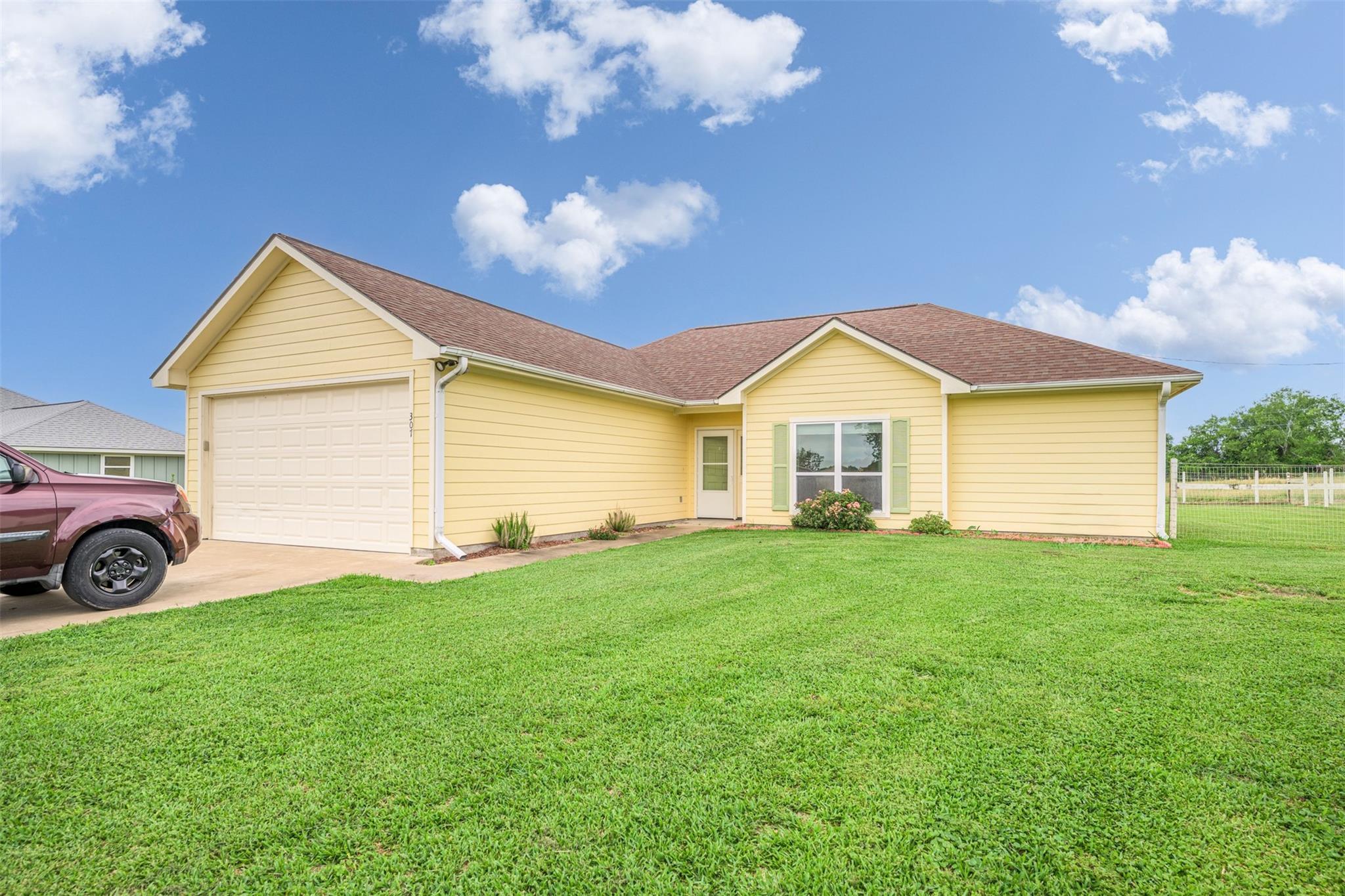 Pale yellow single-story home with an attached garage, broad green lawn, and a pickup in the driveway.