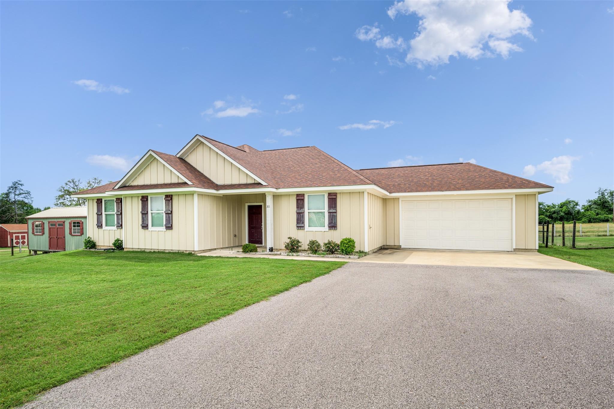 Cream-colored single-story home with an attached garage, gravel driveway, and small outbuilding.
