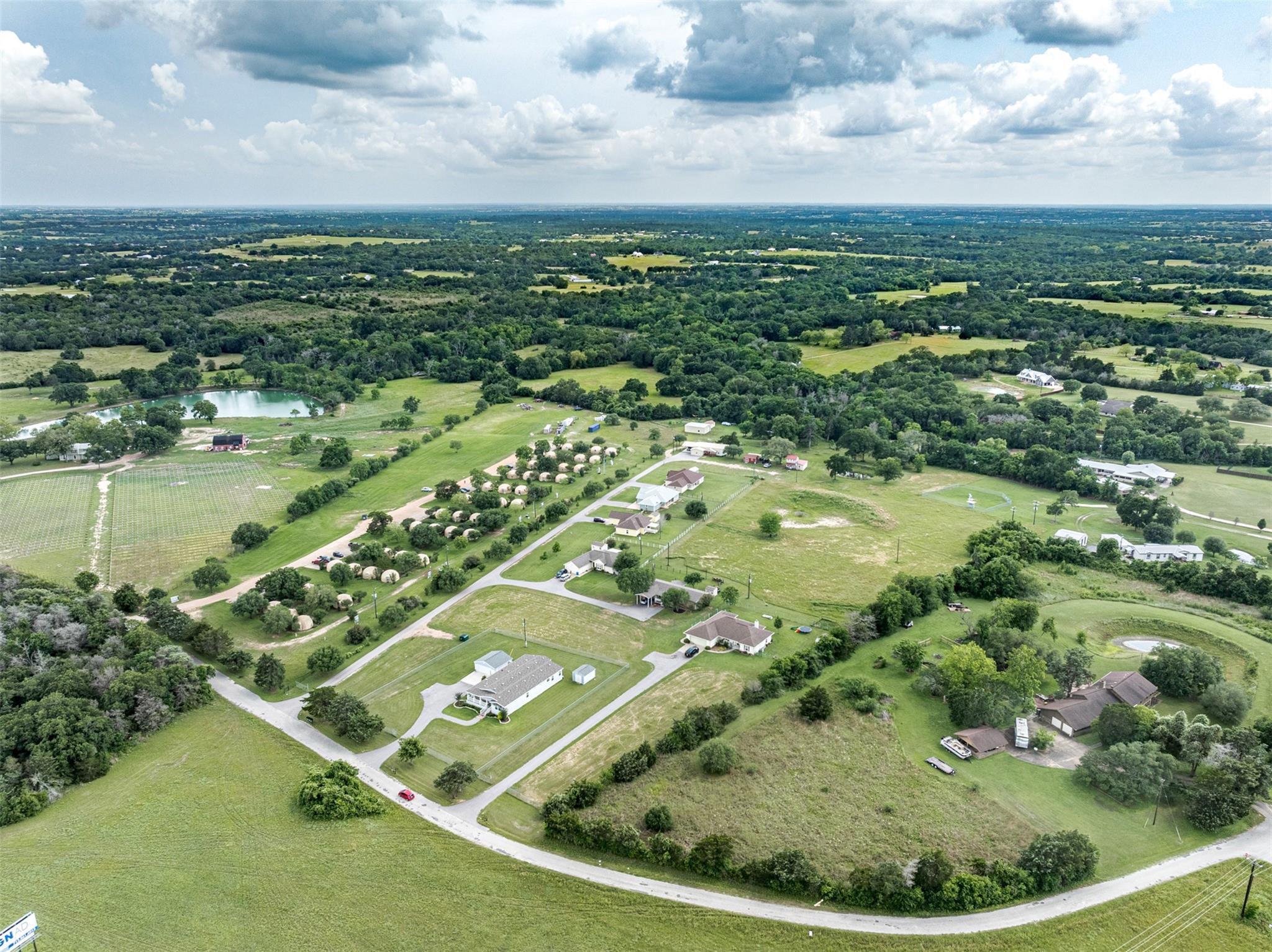 Aerial view of rural homes and open fields, with a pond and winding roads.