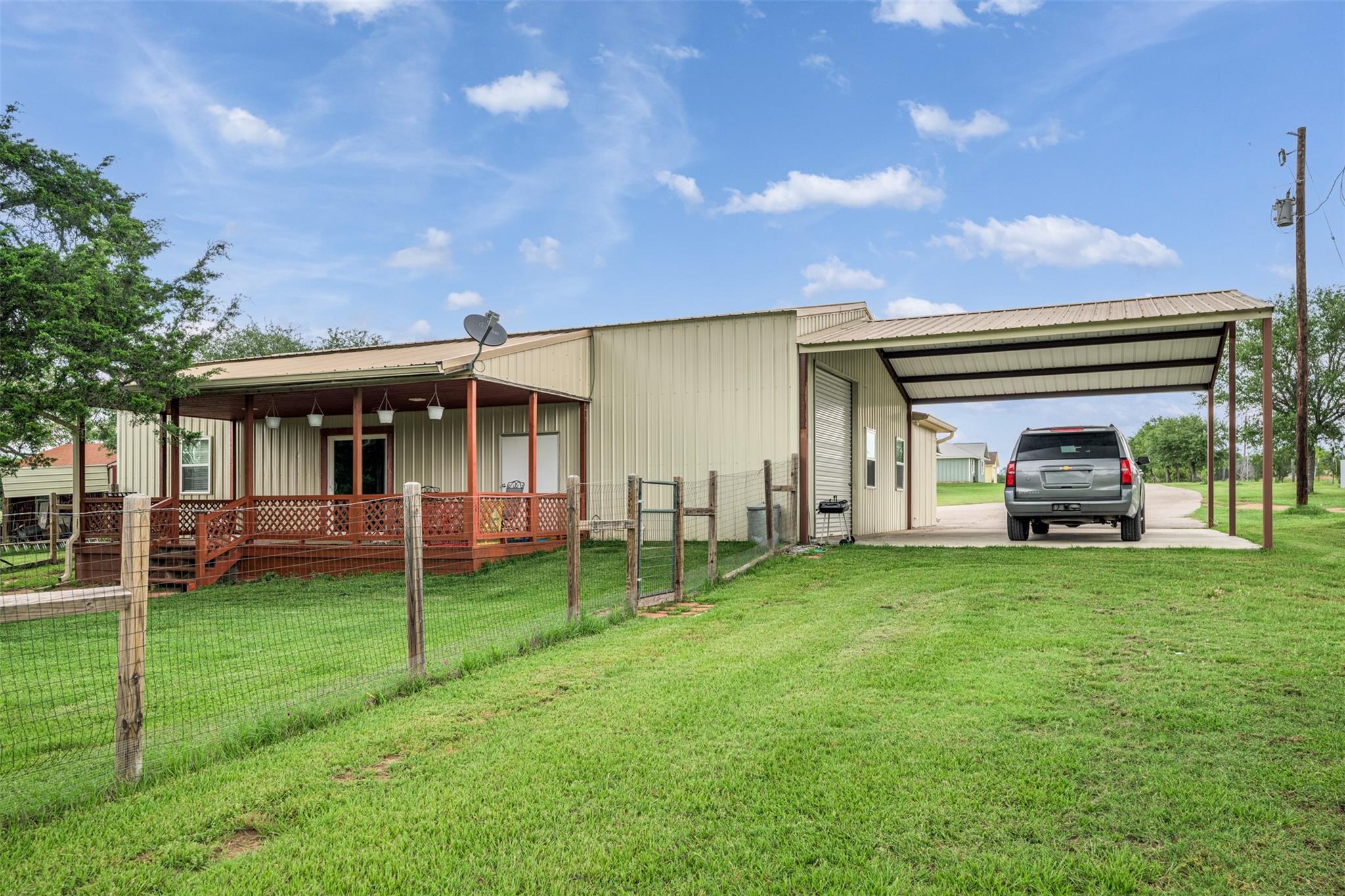 Metal-sided home with a covered porch, carport, parked SUV, and fenced lawn.