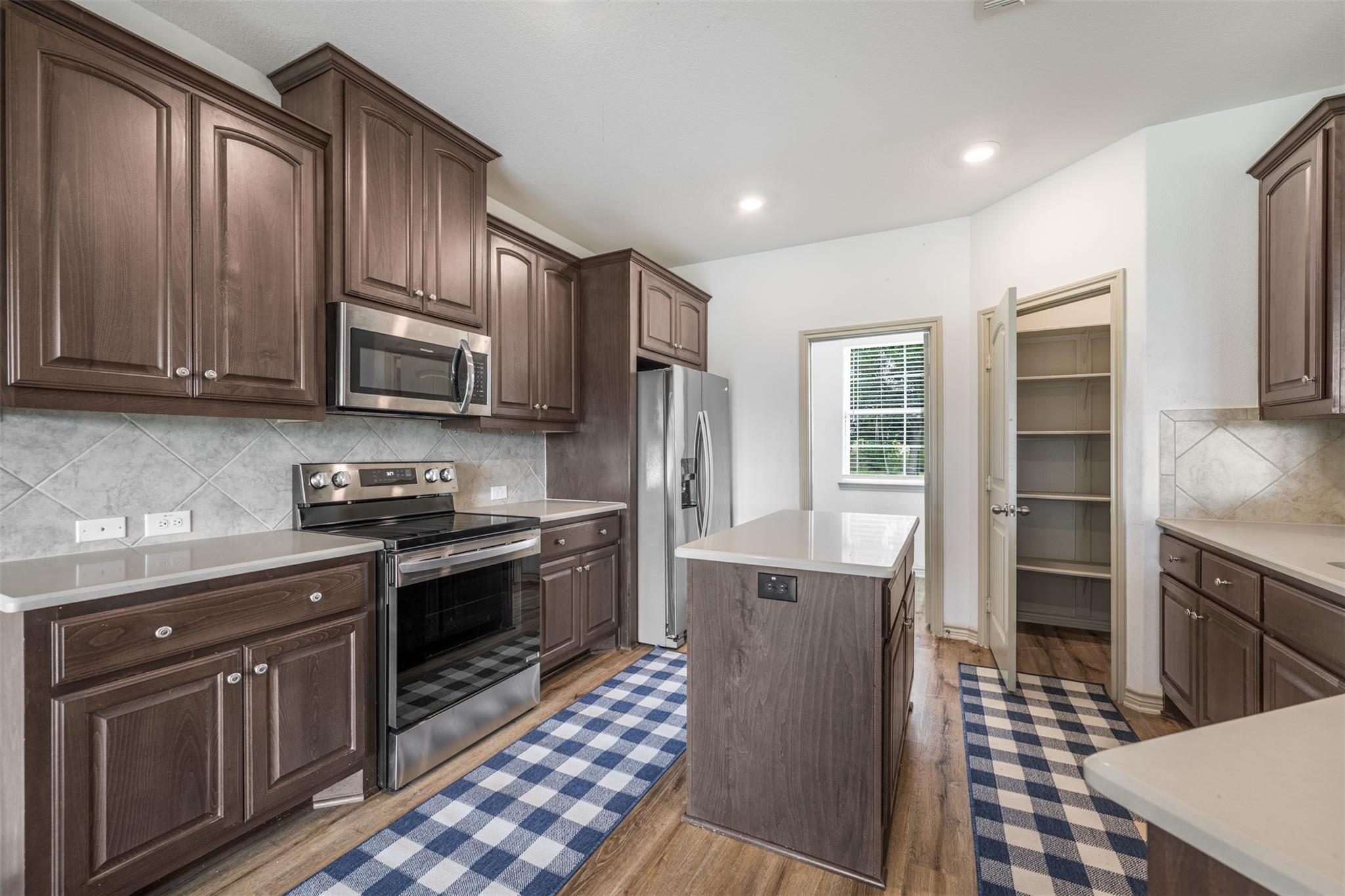 Kitchen with dark wood cabinets, stainless steel appliances, central island, and an open pantry.