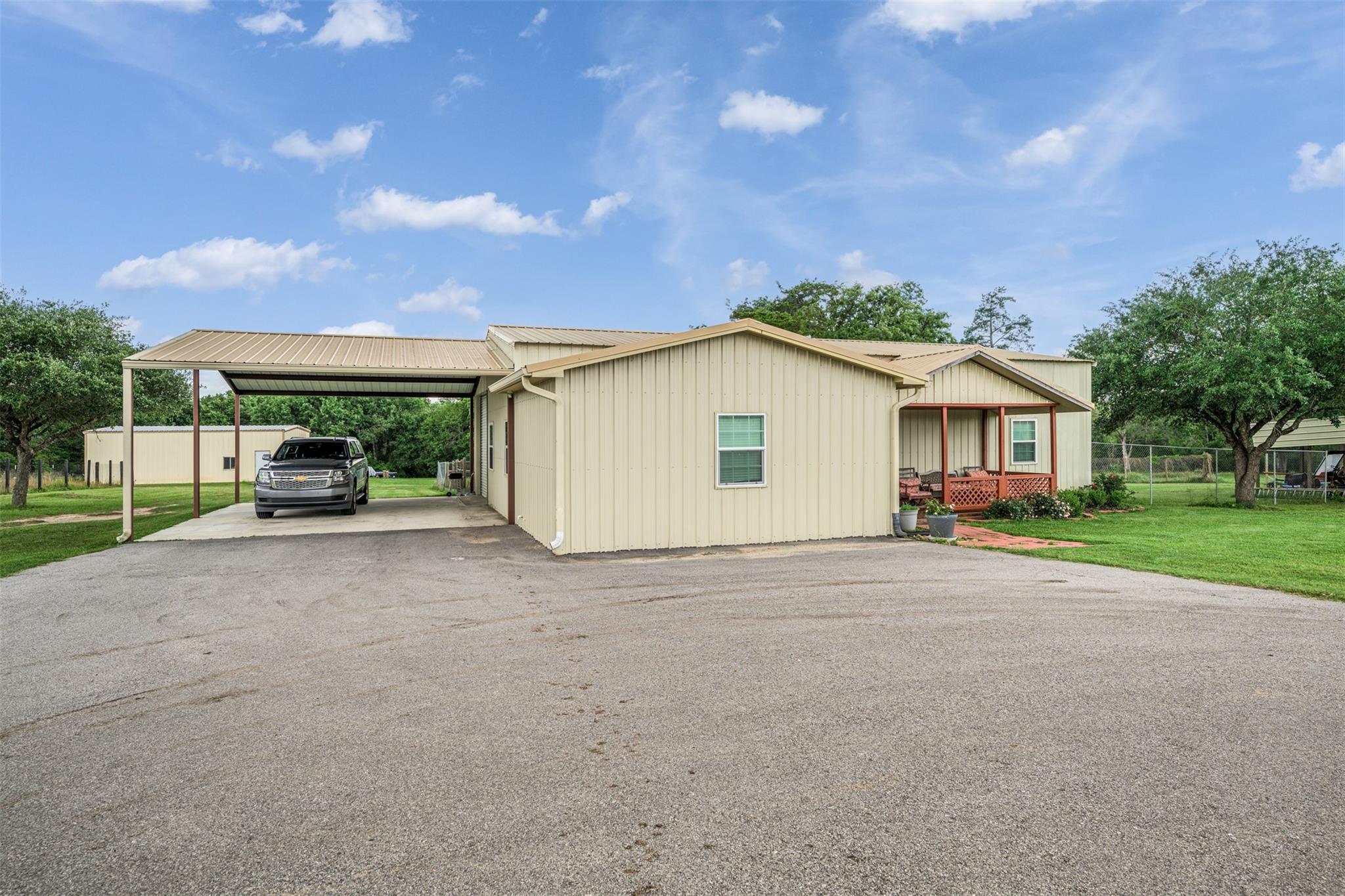 Beige metal-sided home with a covered carport, porch, and wide paved driveway.