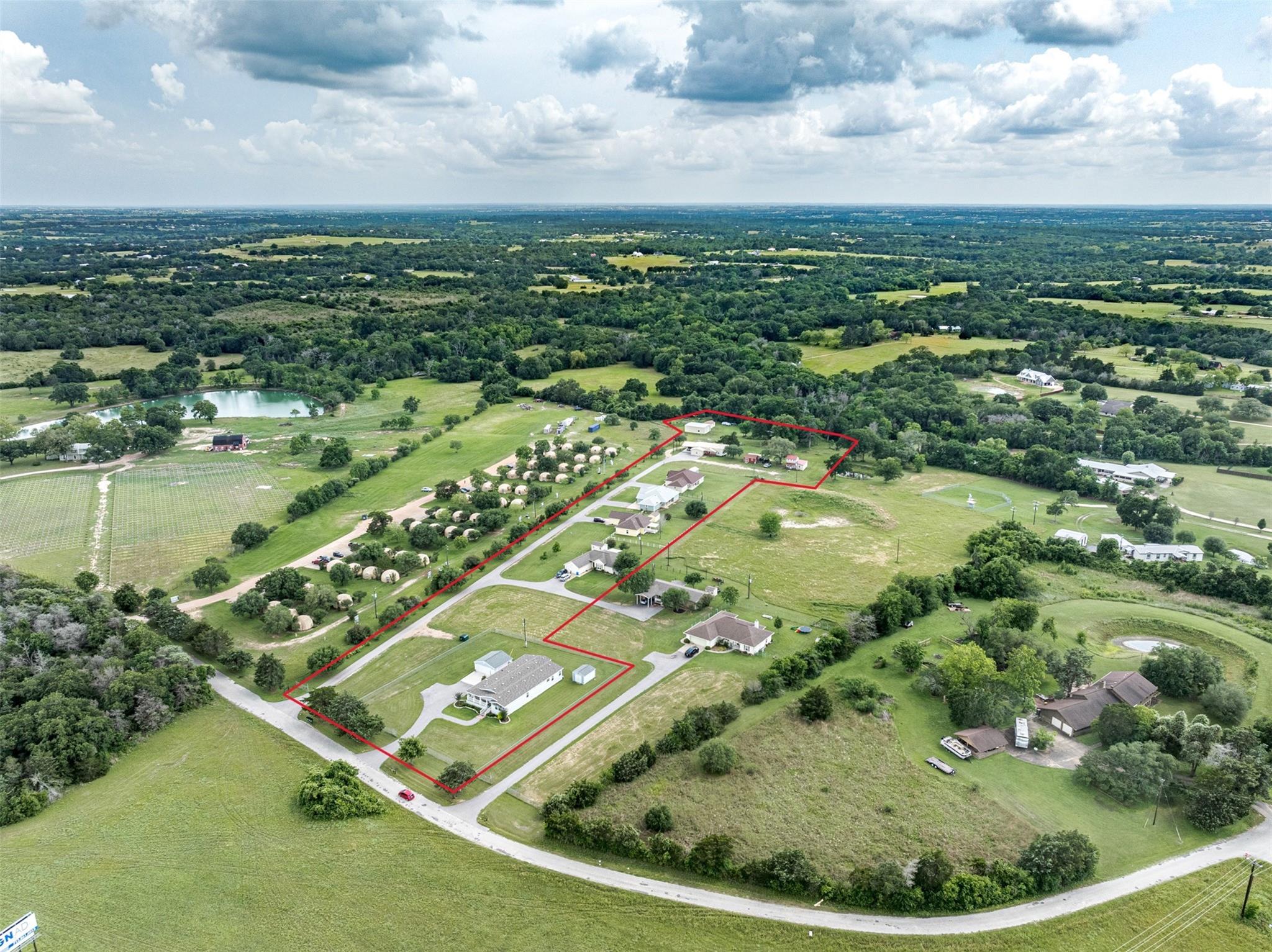 Aerial view of a red-outlined rural property with several homes and outbuildings along a private drive.
