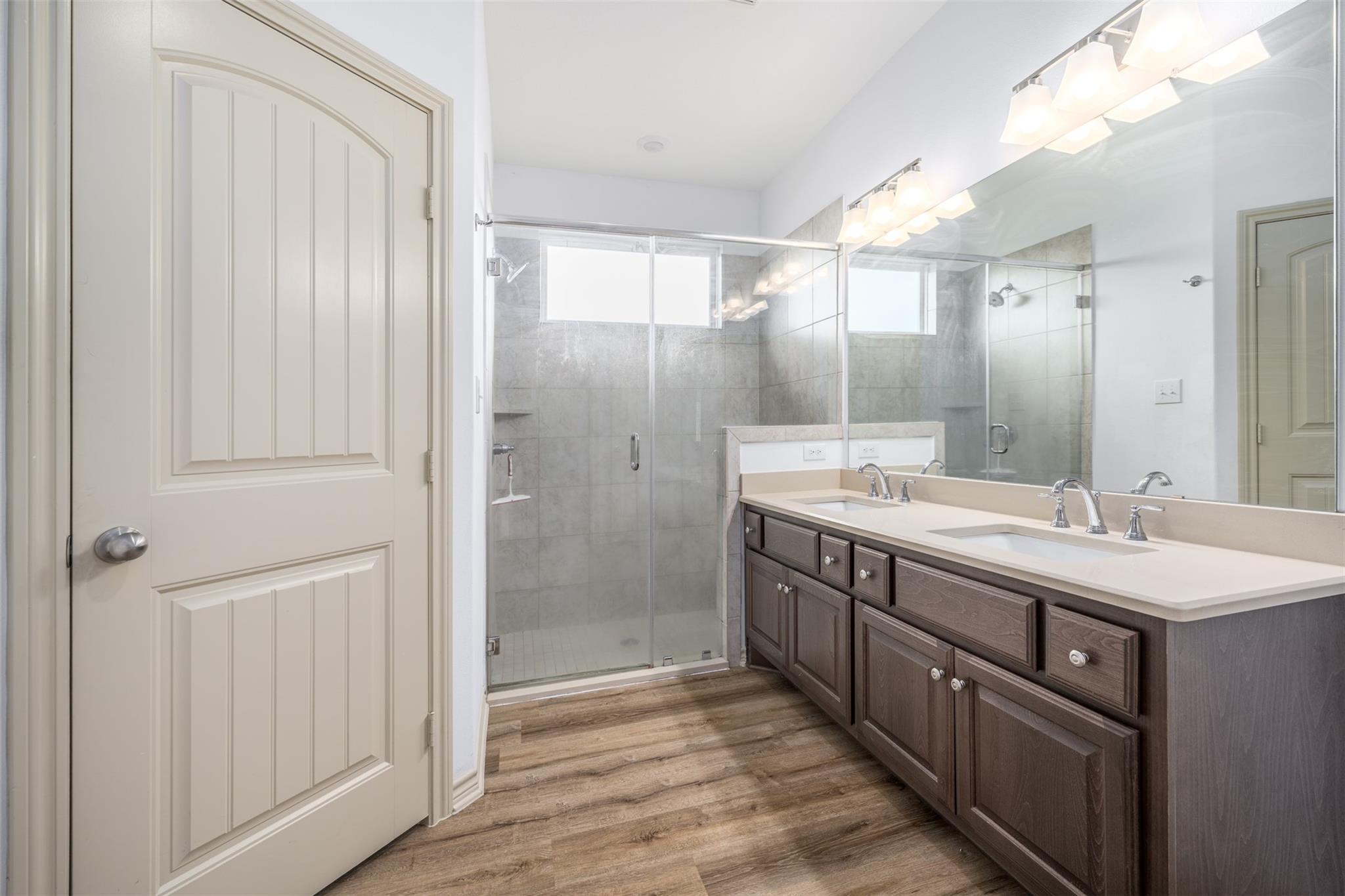 Bathroom with double-sink vanity, large mirror, and glass-enclosed gray tile shower.