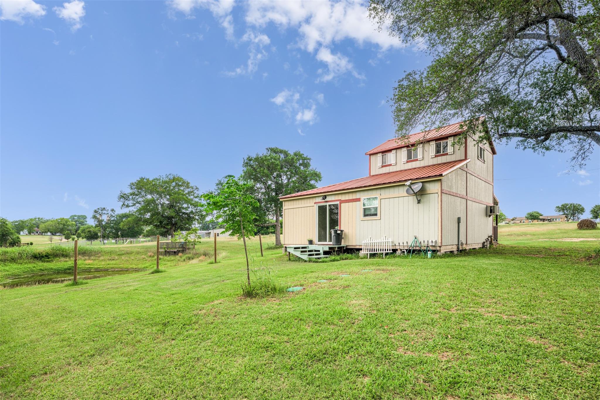 Two-story home with red metal roofs in a grassy yard beneath mature trees.