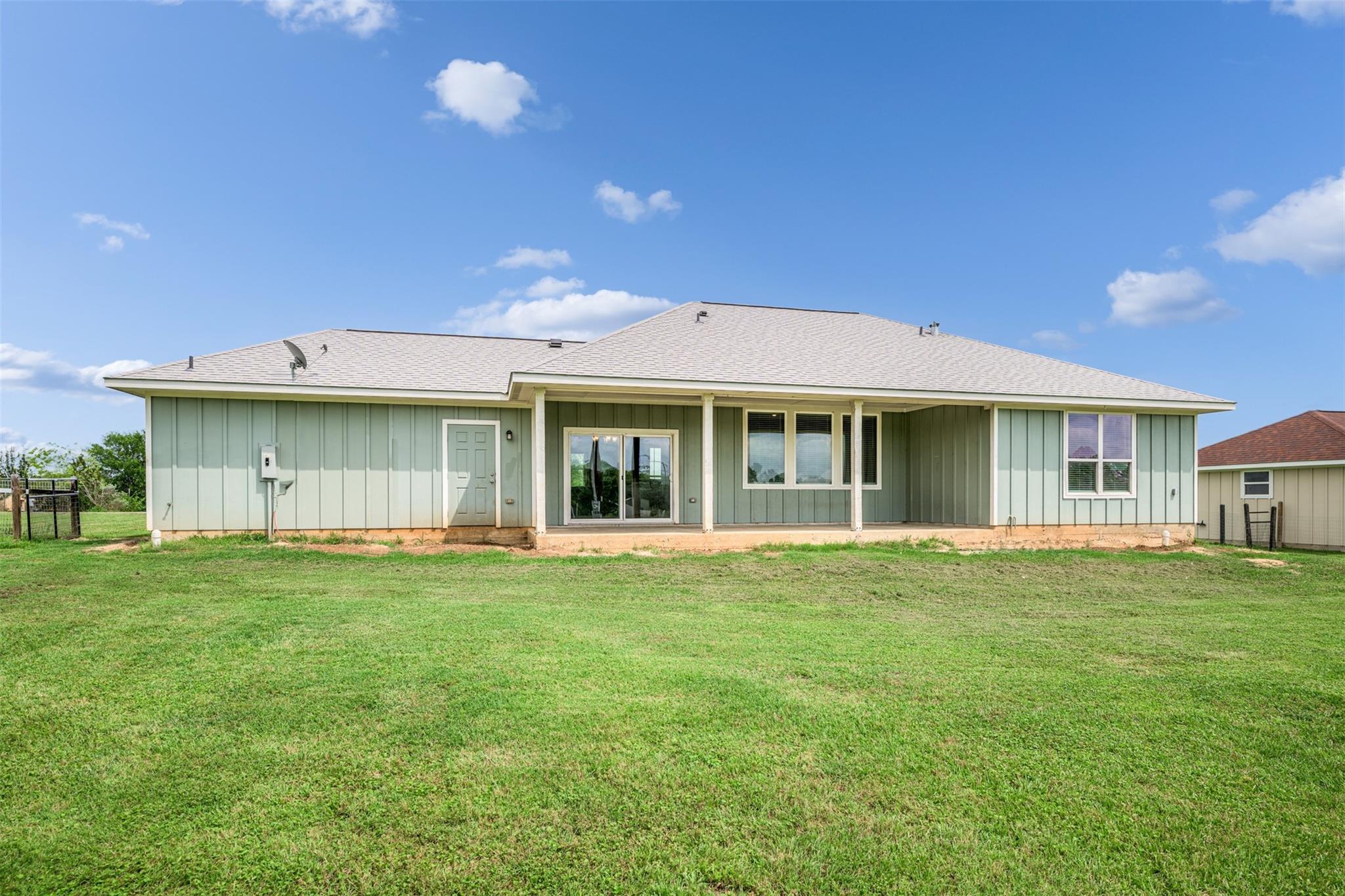 Rear of a pale green single-story home with a covered patio and broad lawn.