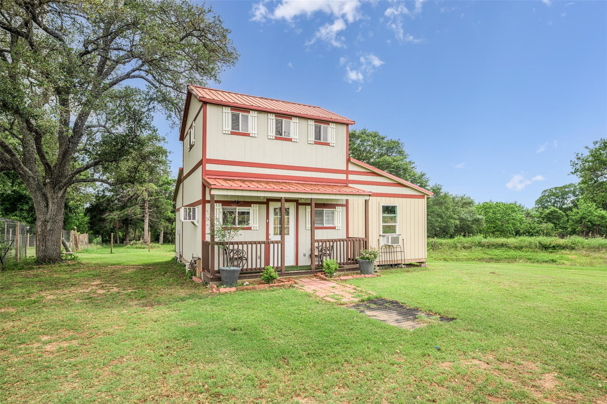 Two-story cream house with red trim, a covered porch, and a broad lawn.