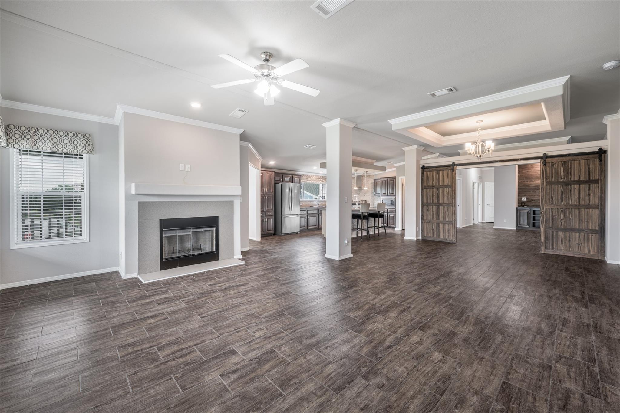 Open living area with a tiled fireplace, dark wood-look floors, and rustic sliding barn doors.
