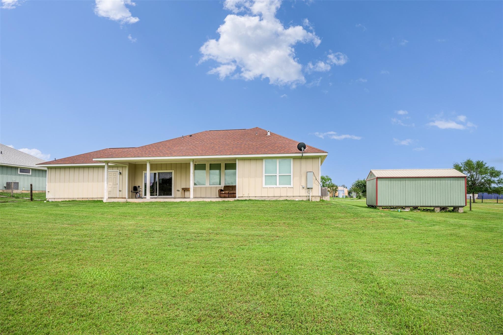 Rear exterior of a beige single-story home with a covered patio and detached shed.