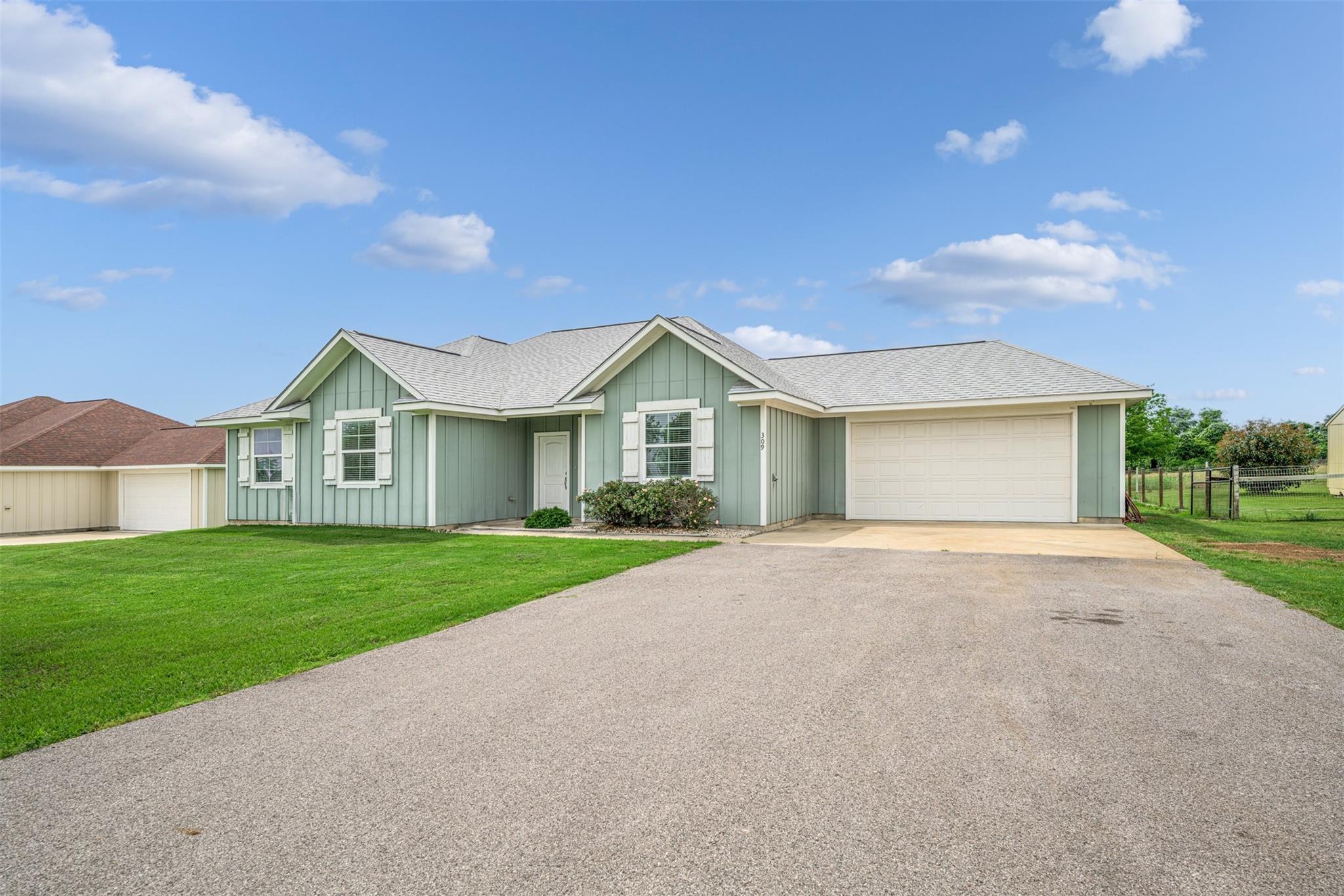 Sage-green house with white trim, attached garage, broad driveway, and green lawn.
