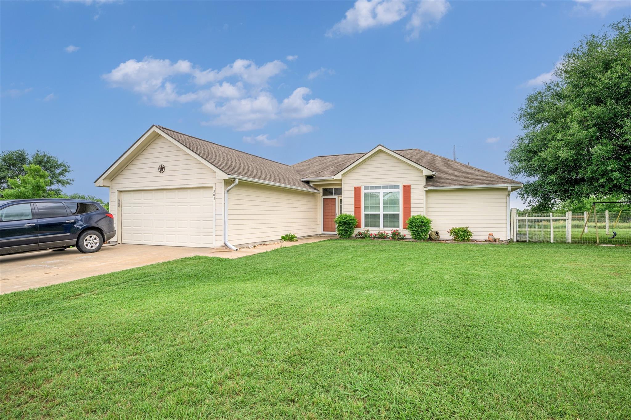 Single-story beige home with a two-car garage, red shutters, and a wide green lawn.
