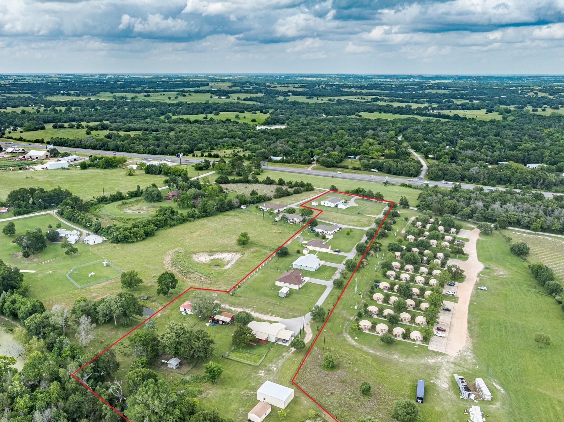 Aerial view of red-outlined property with several buildings, open land, and a nearby highway.