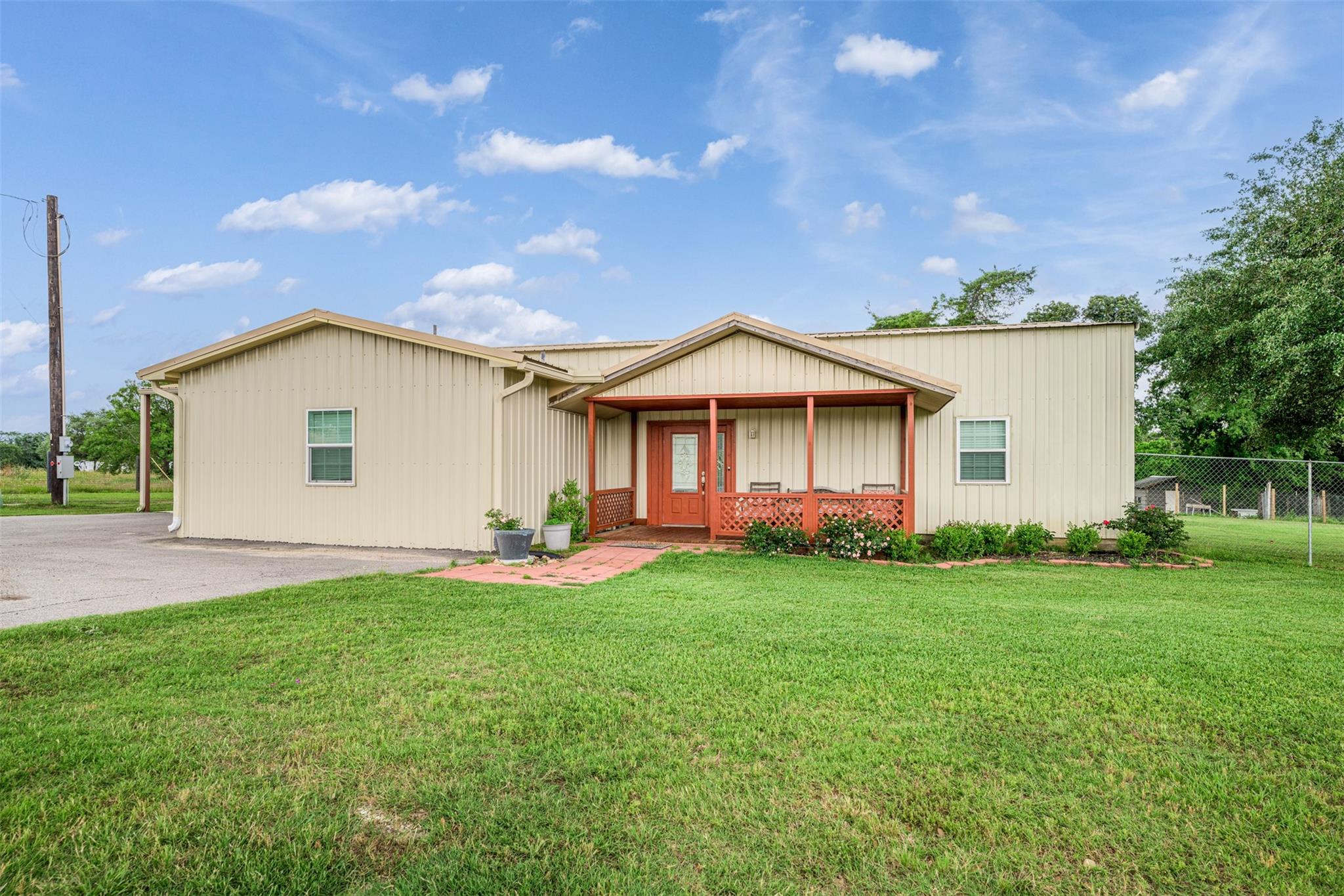 Cream-colored single-story home with a red-trimmed covered porch and broad green lawn.