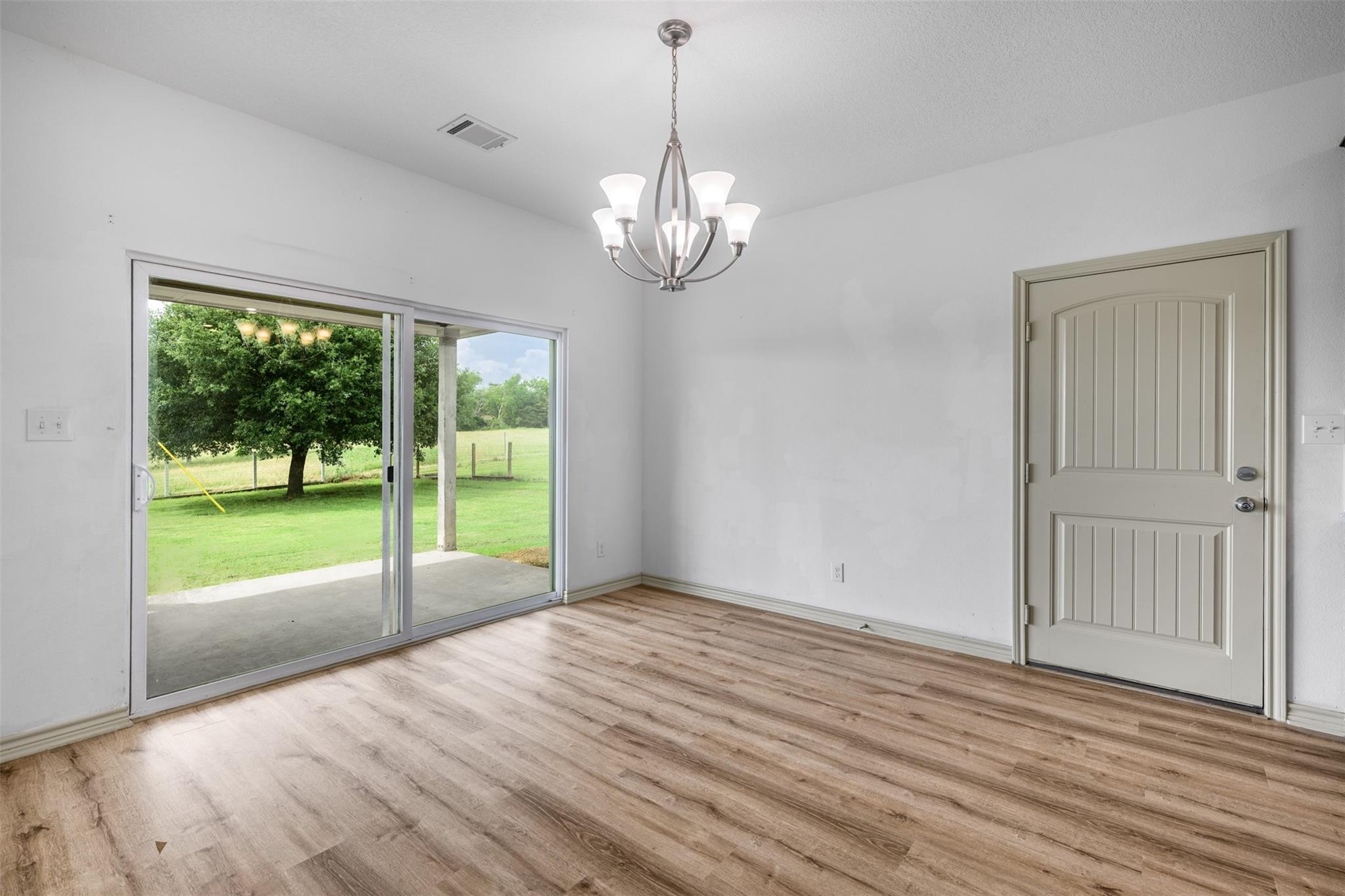Empty room with wood-look floors, a chandelier, and sliding doors to a covered patio.