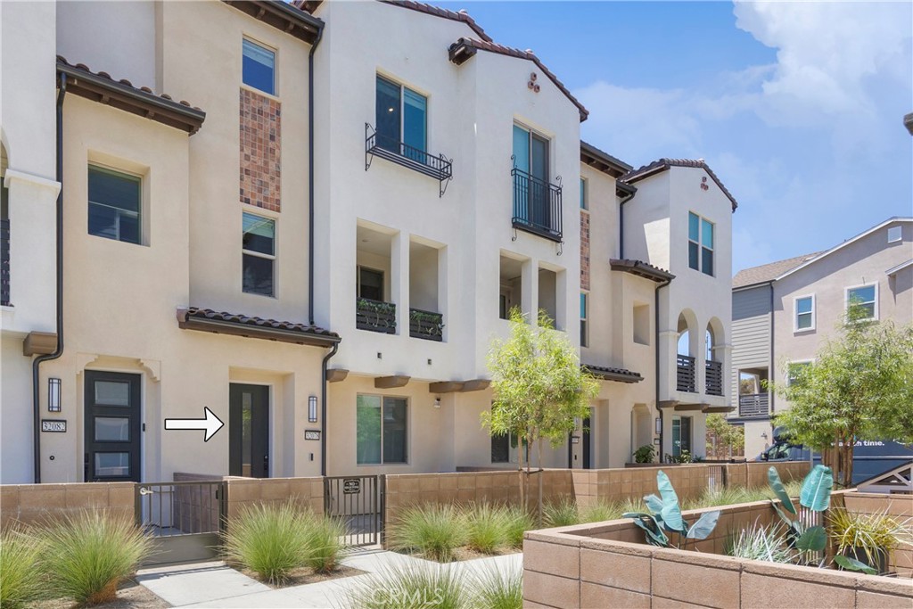 Attached townhouse with light stucco exterior, fenced patios, and an arrow pointing to a ground-floor door.
