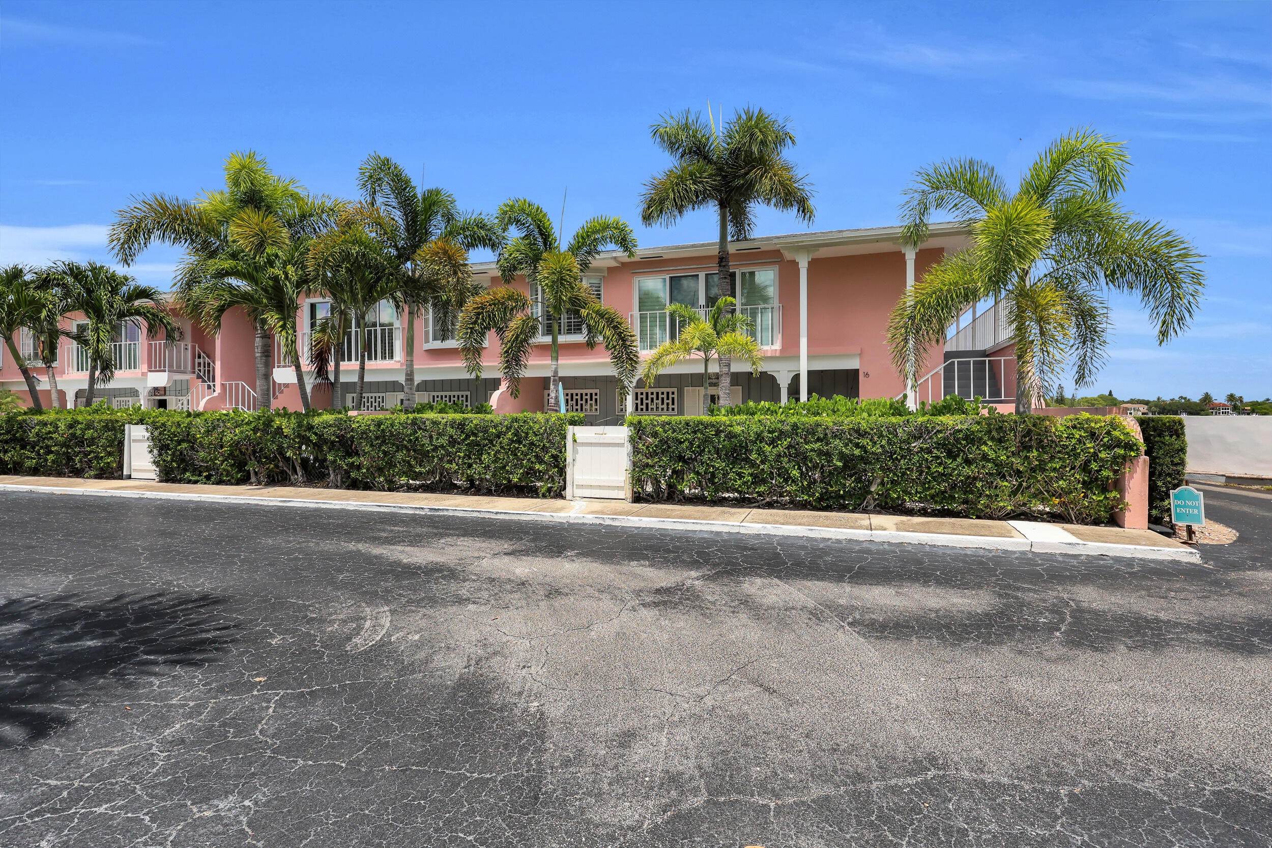 Pink two-story residential building with white balconies and palm trees behind a hedge.