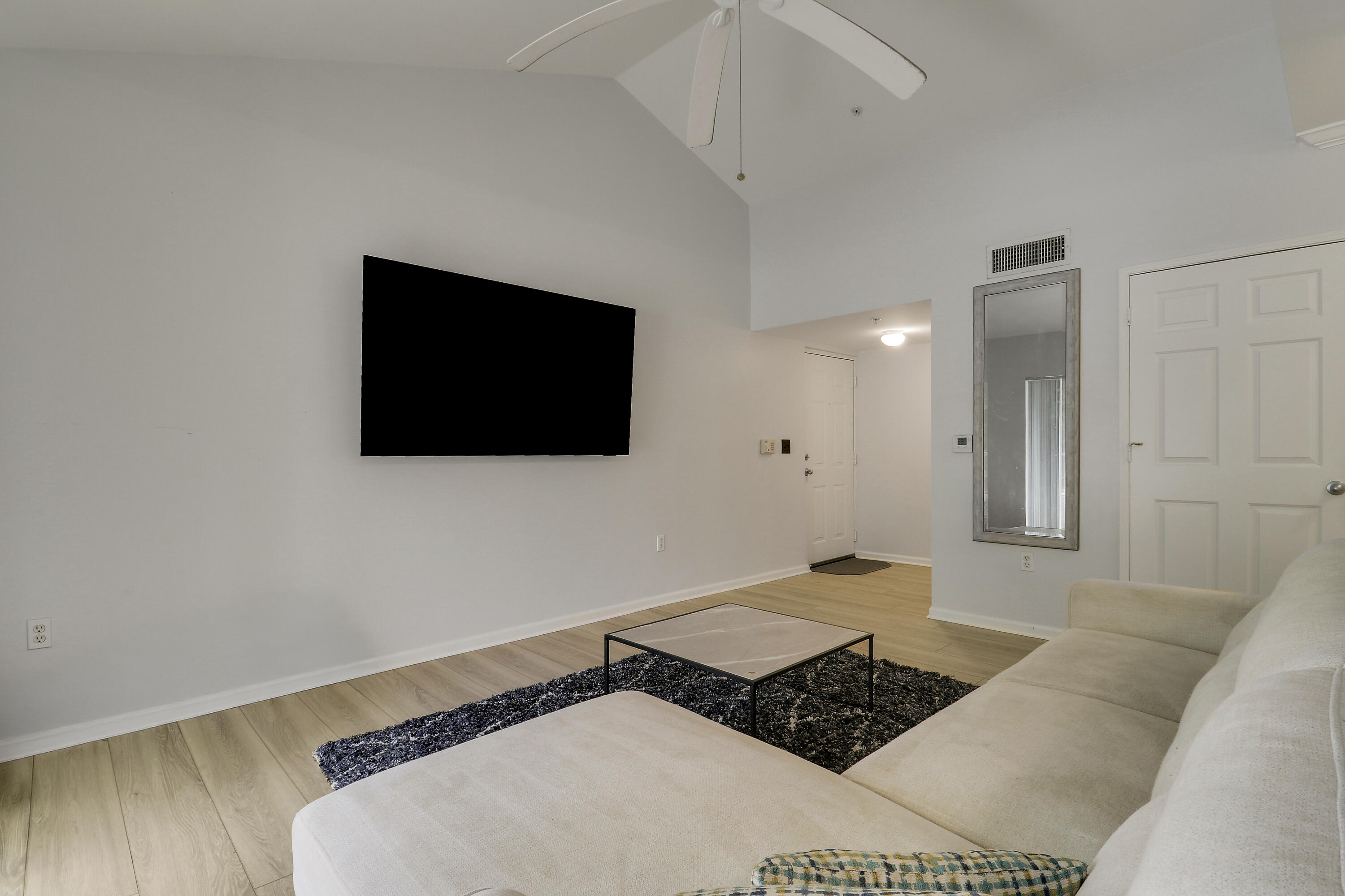 Living room with a vaulted ceiling, wall-mounted television, and light sectional sofa.