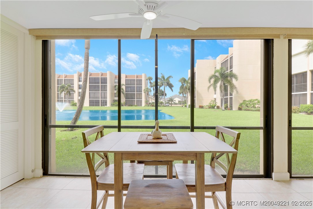 Dining table facing sliding glass doors with a view of a palm-lined lawn and water.