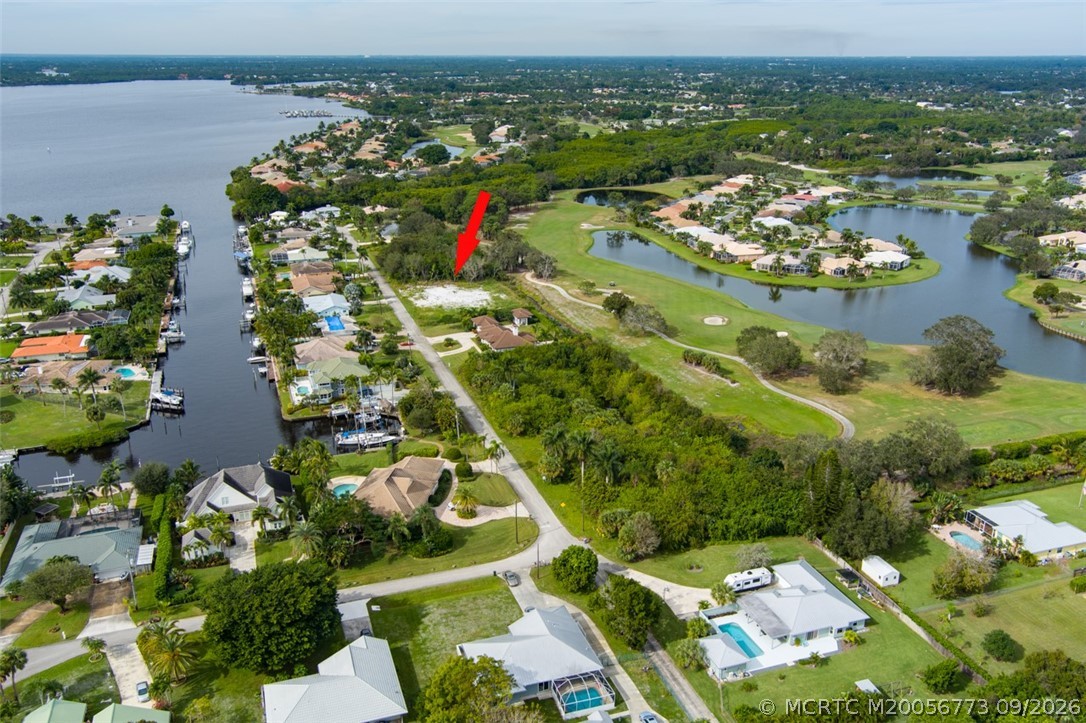 Aerial view of vacant lot marked by red arrow beside golf course and canal.