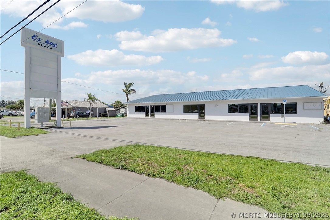 Single-story commercial building with a blue metal roof and tall plaza sign beside the parking lot.