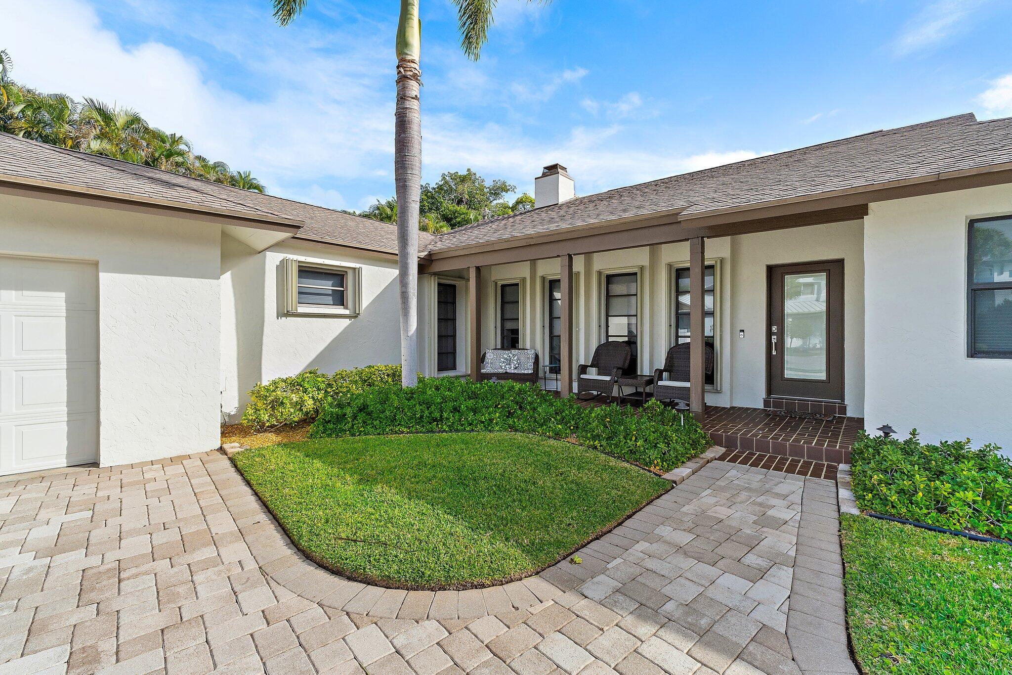 White stucco home with a covered porch, palm tree, and landscaped paver courtyard.