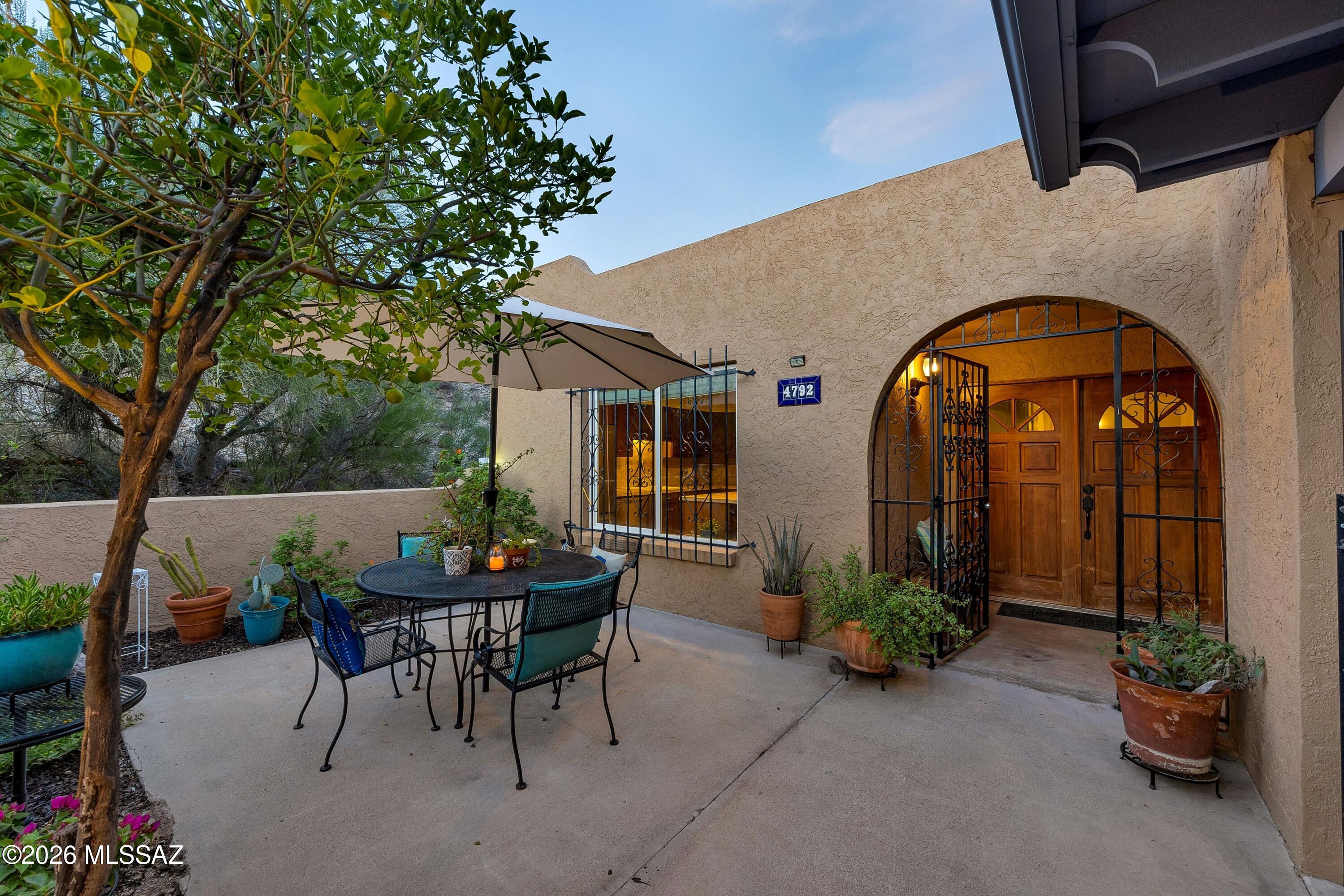 Home courtyard with an arched wrought-iron entry, wooden double doors, and a shaded patio dining set.